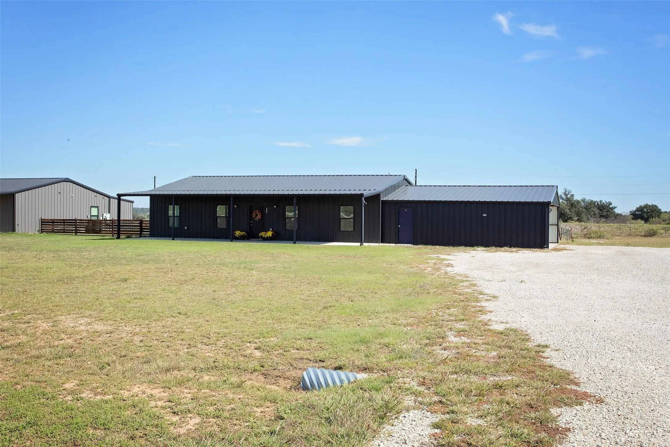 Dark-toned metal siding exterior featuring a full-length covered porch, metal roofing, attached side structure, and expansive open-ground acreage