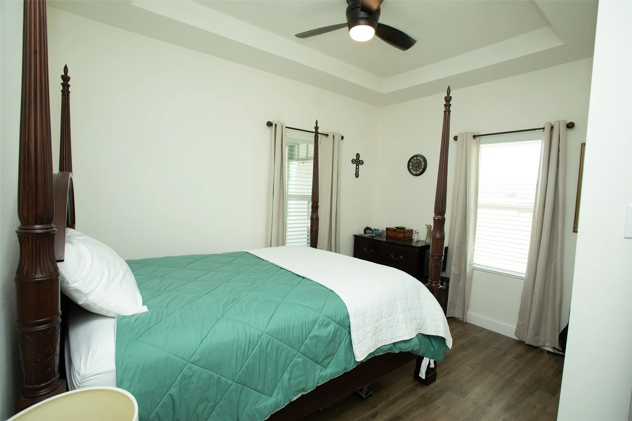 Tray ceiling with integrated ceiling fan, wood-finish flooring, and dual windows