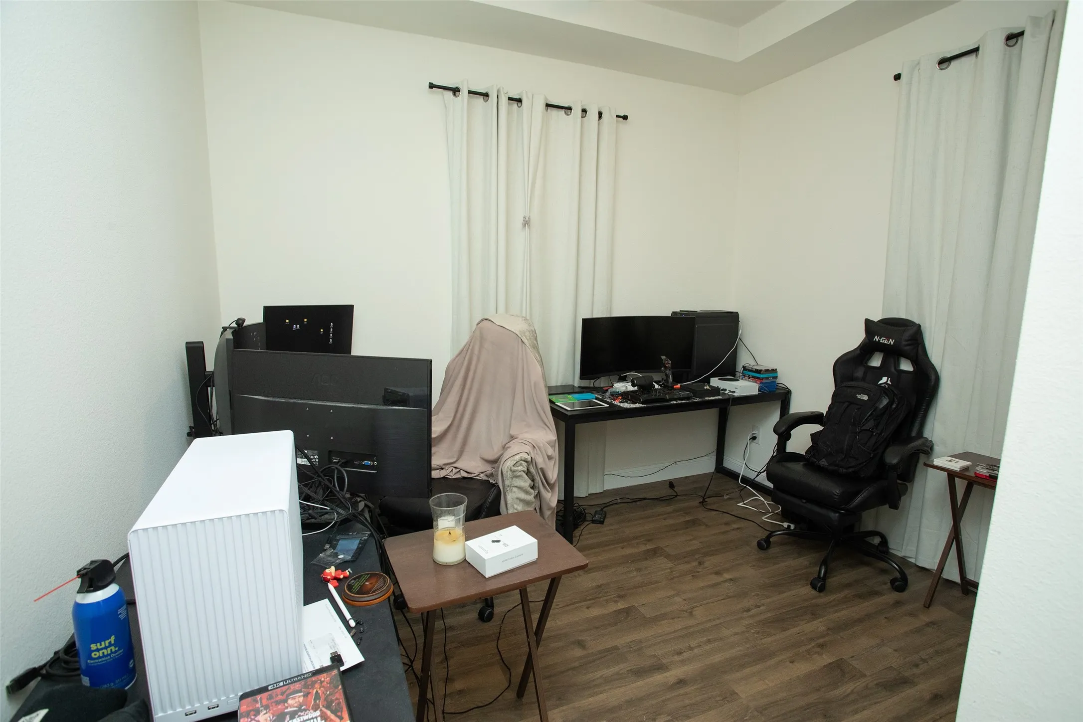 Room featuring wood-finish flooring, recessed tray ceiling, and dual windows with curtain rod hardware