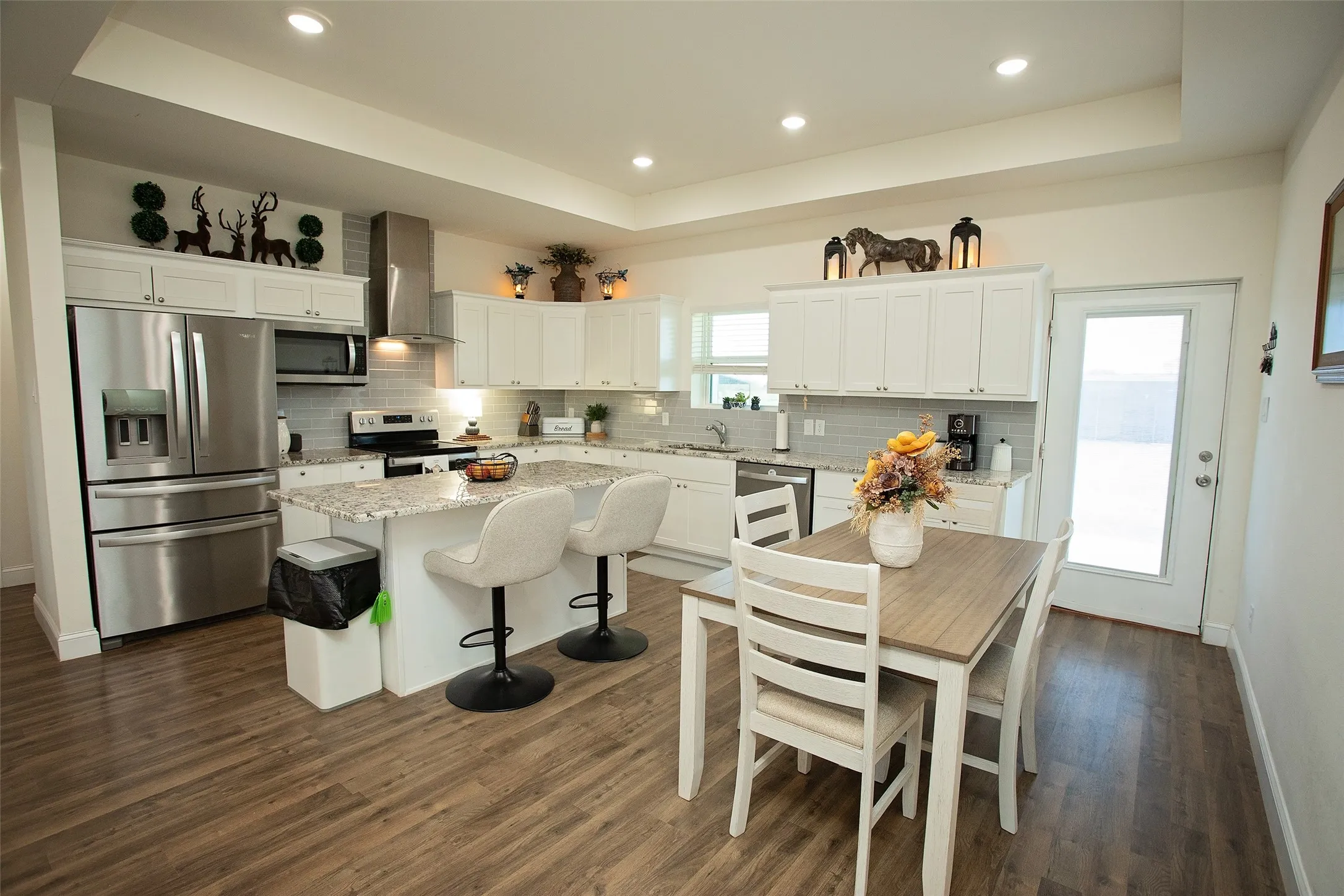 Kitchen featuring white shaker-style cabinetry, stainless steel appliances, stone-surface countertops, wood-finish flooring, and a tray ceiling with recessed lighting