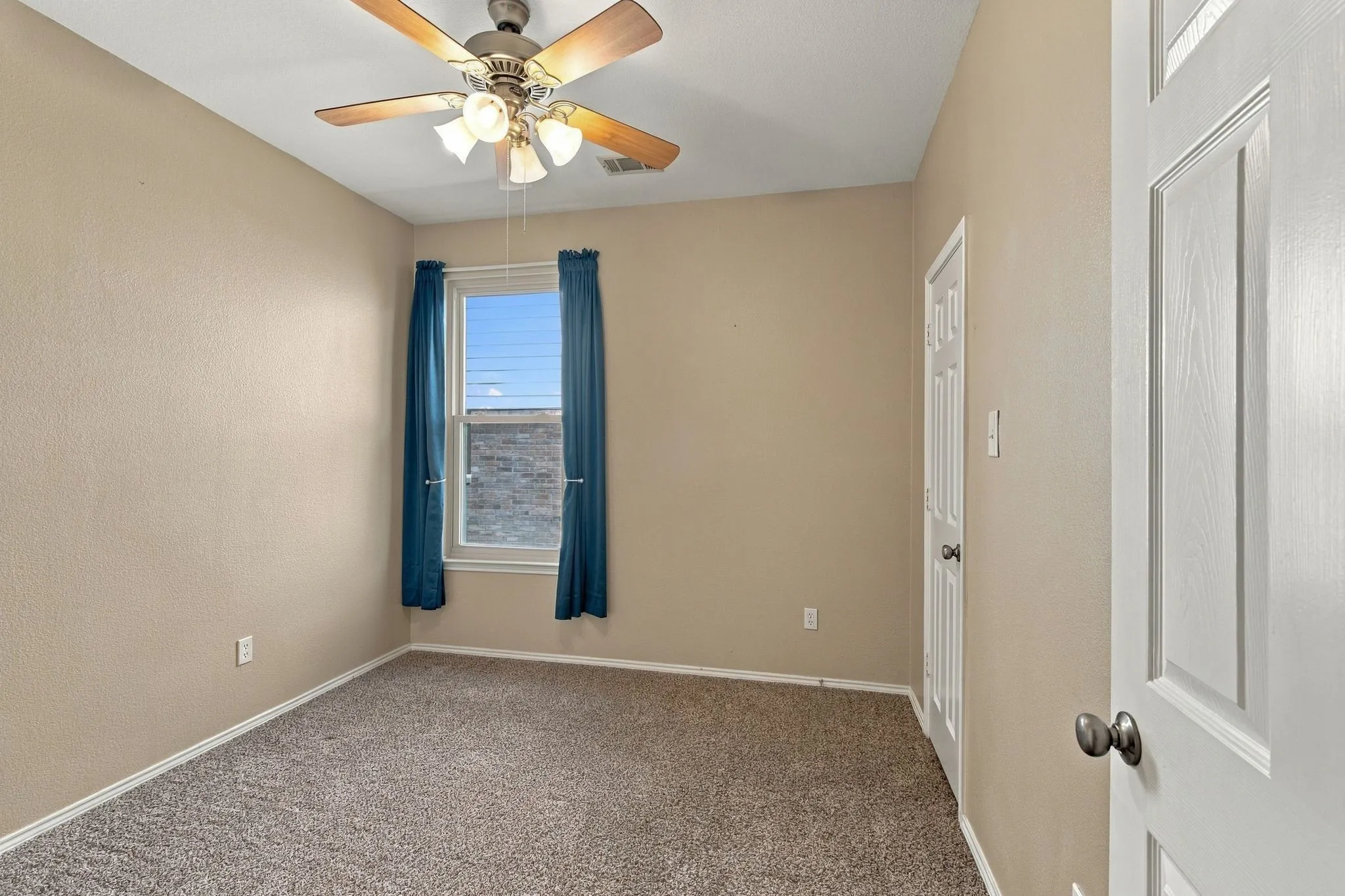 Neutral wall-to-wall carpeting, ceiling fan with multi-light fixture, and single-hung window with natural light