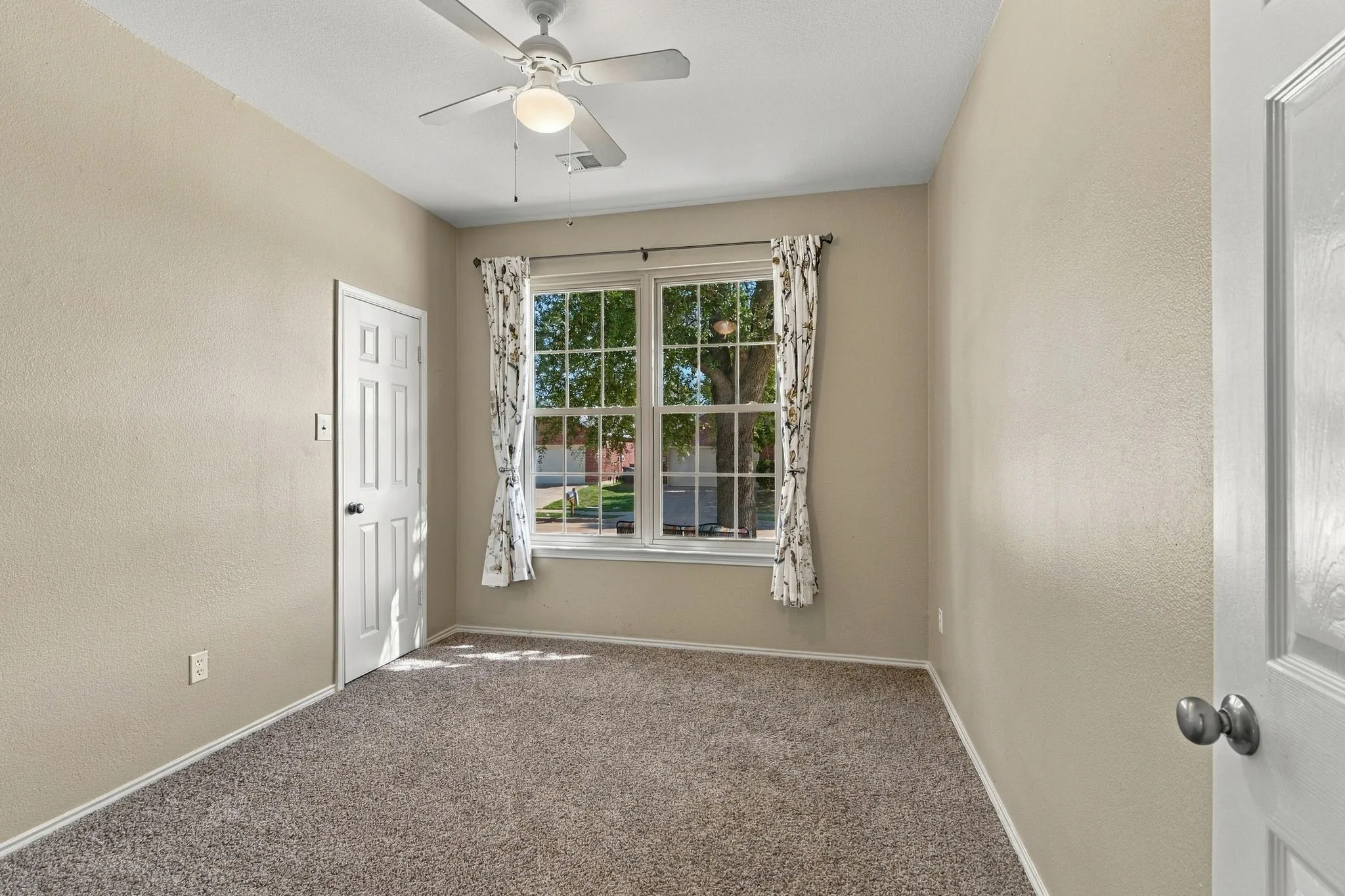 Room featuring neutral wall tones, wall-to-wall carpeting, dual-pane windows with grid detailing, and a central ceiling fan with an integrated light fixture