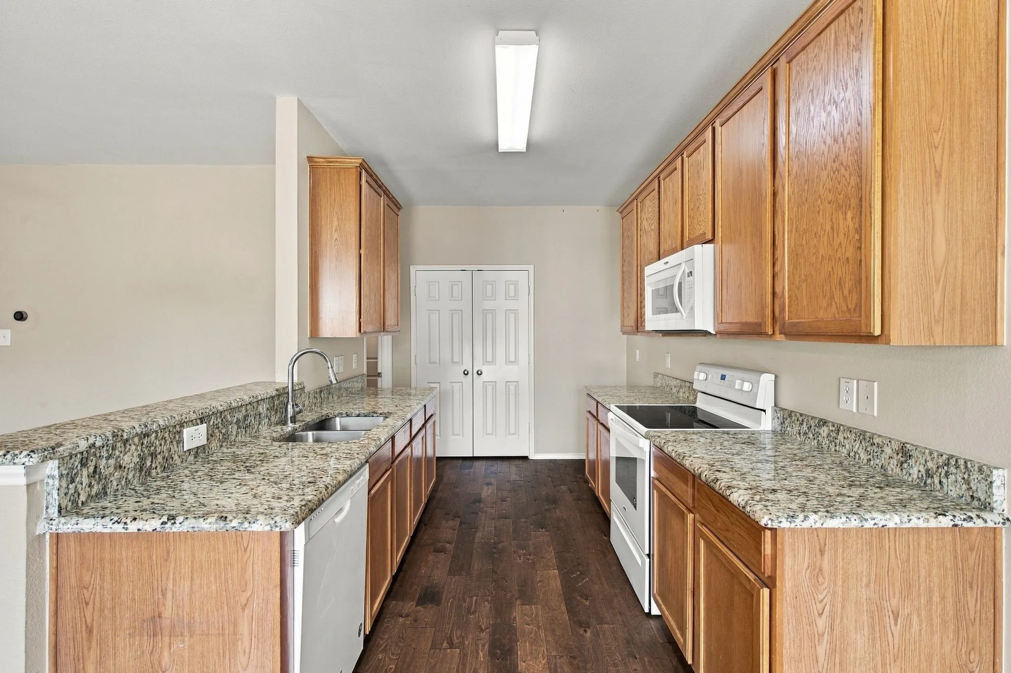 Kitchen featuring wood-finish cabinetry, stone-patterned countertops, wood-finish flooring, a stainless steel double-basin sink, and a built-in microwave