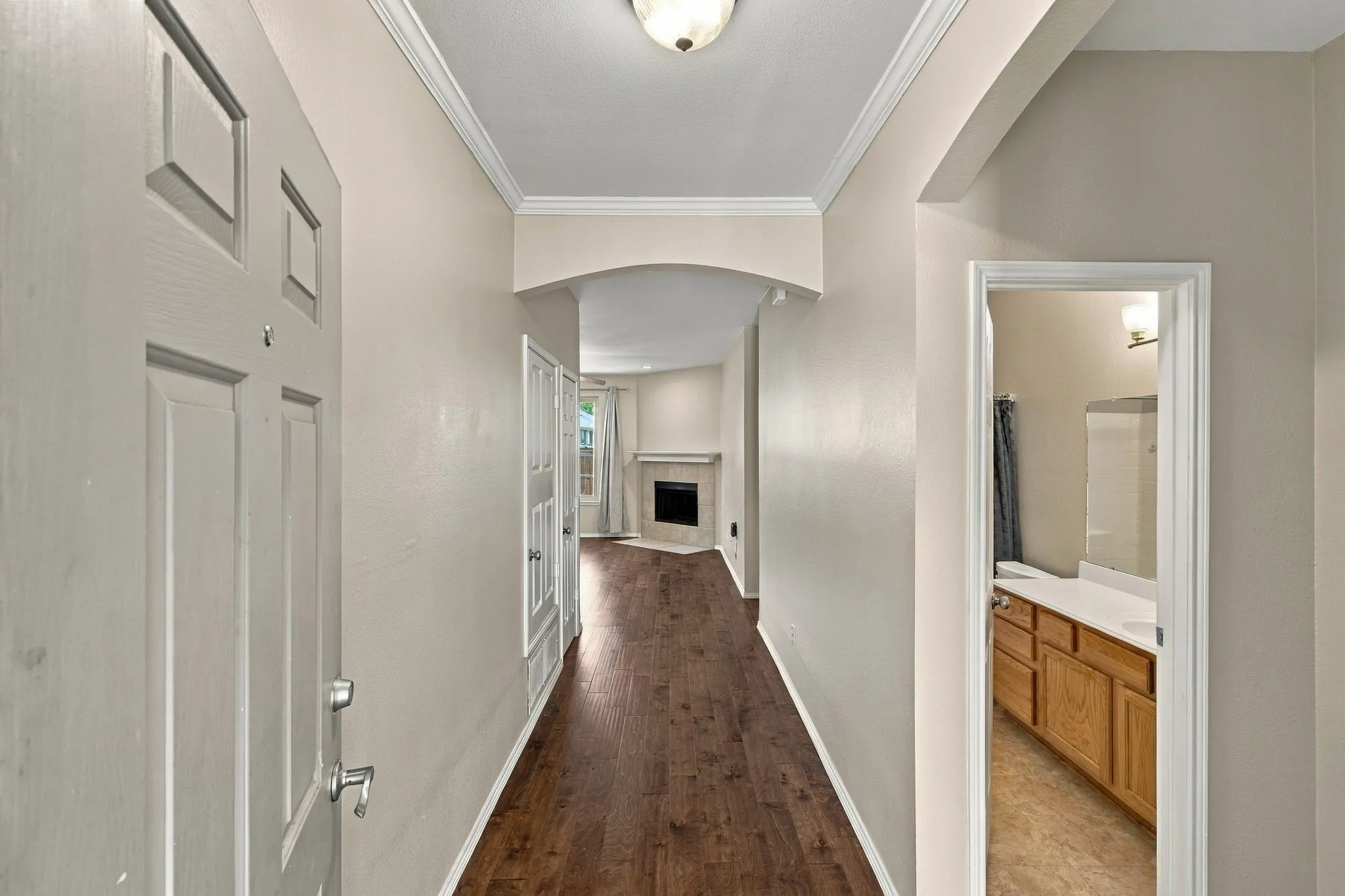 Interior entryway featuring wood-finish flooring, crown molding, arched architectural detailing, a fireplace with a stone-finish surround, and a bathroom equipped with wood cabinetry and a wall-mounted vanity mirror