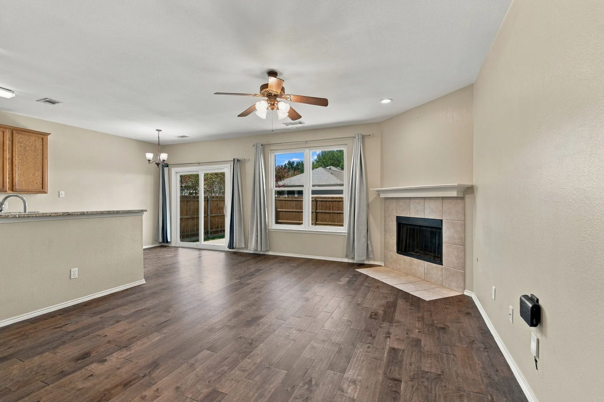 Living area featuring wood-finish flooring, a corner fireplace with a stone-surround mantel, ceiling fan, sliding glass doors, and a breakfast bar