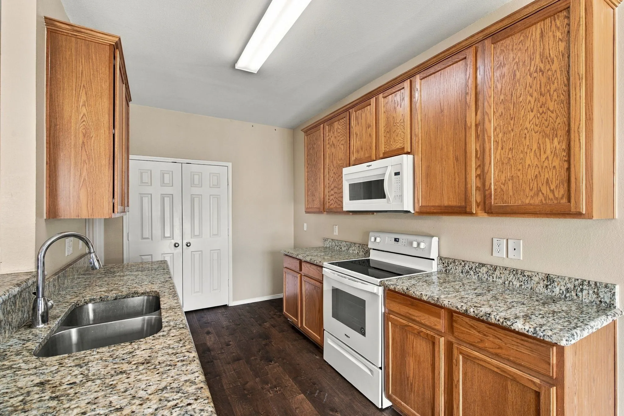 Kitchen featuring wood cabinetry, stone-finish countertops, wood-finish flooring, double-basin stainless steel sink with high-arc faucet, and white appliances