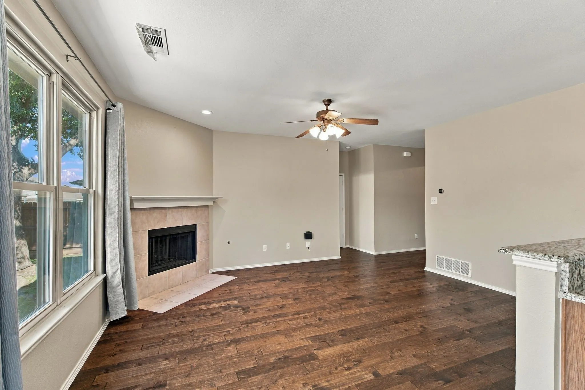 Wood-finish flooring, fireplace with tile surround, ceiling fan, and large windows