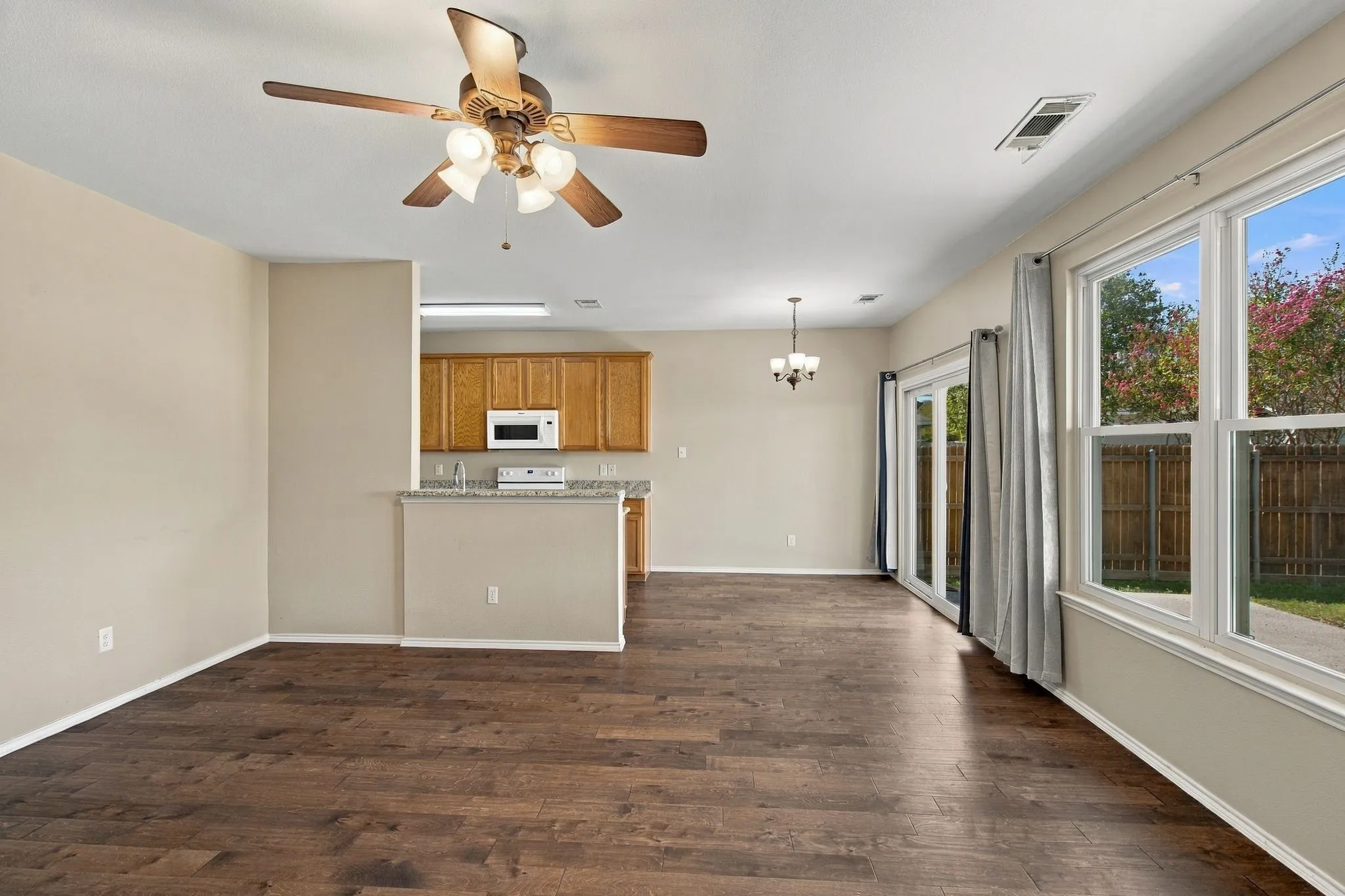 Wood-finish flooring, ceiling fan with integrated lighting, natural stone-finish countertops, cabinetry with neutral-finish hardware, and glass sliding door access to exterior