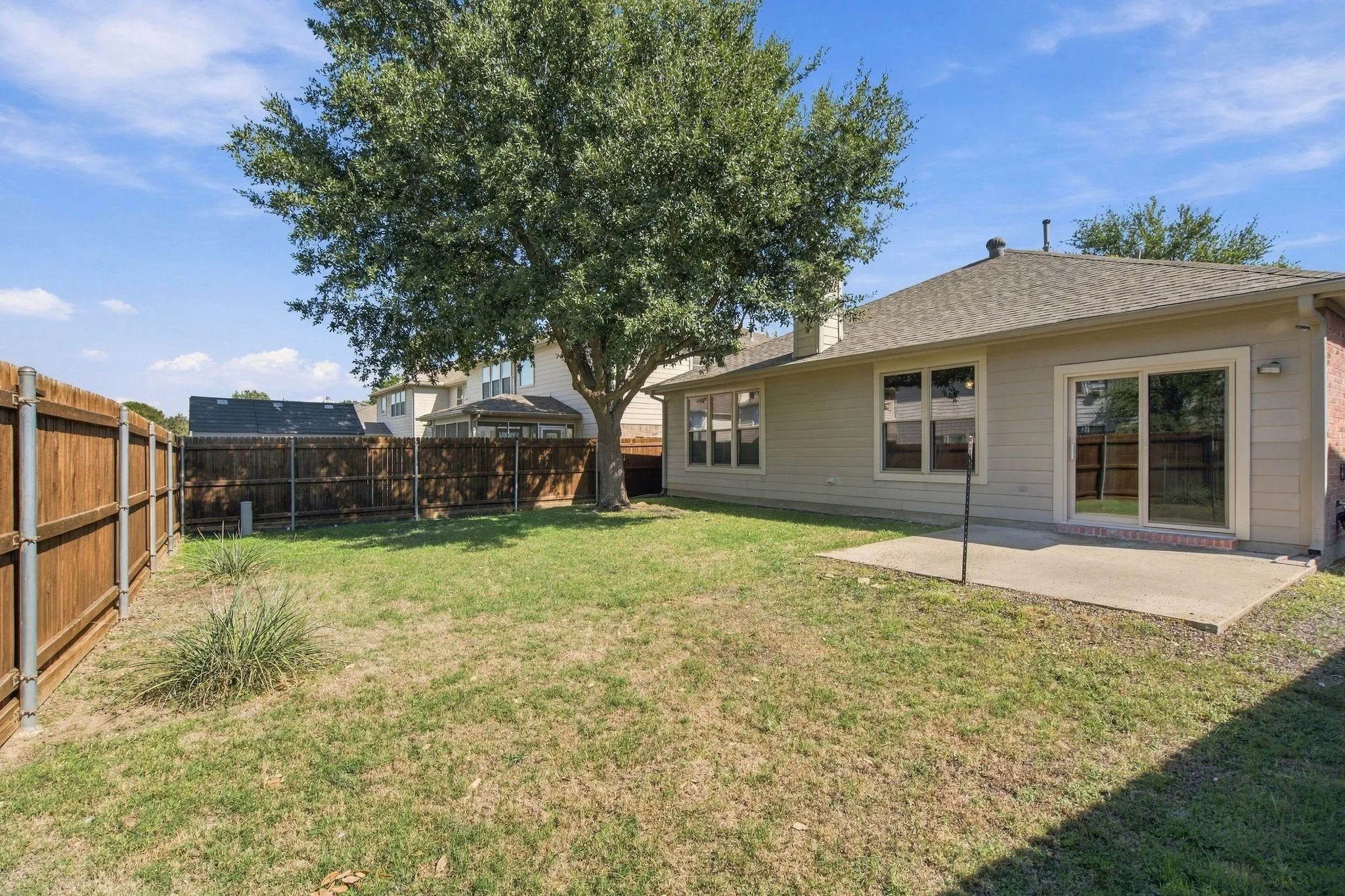 Backyard featuring a concrete patio, wood privacy fencing, and a mature shade tree