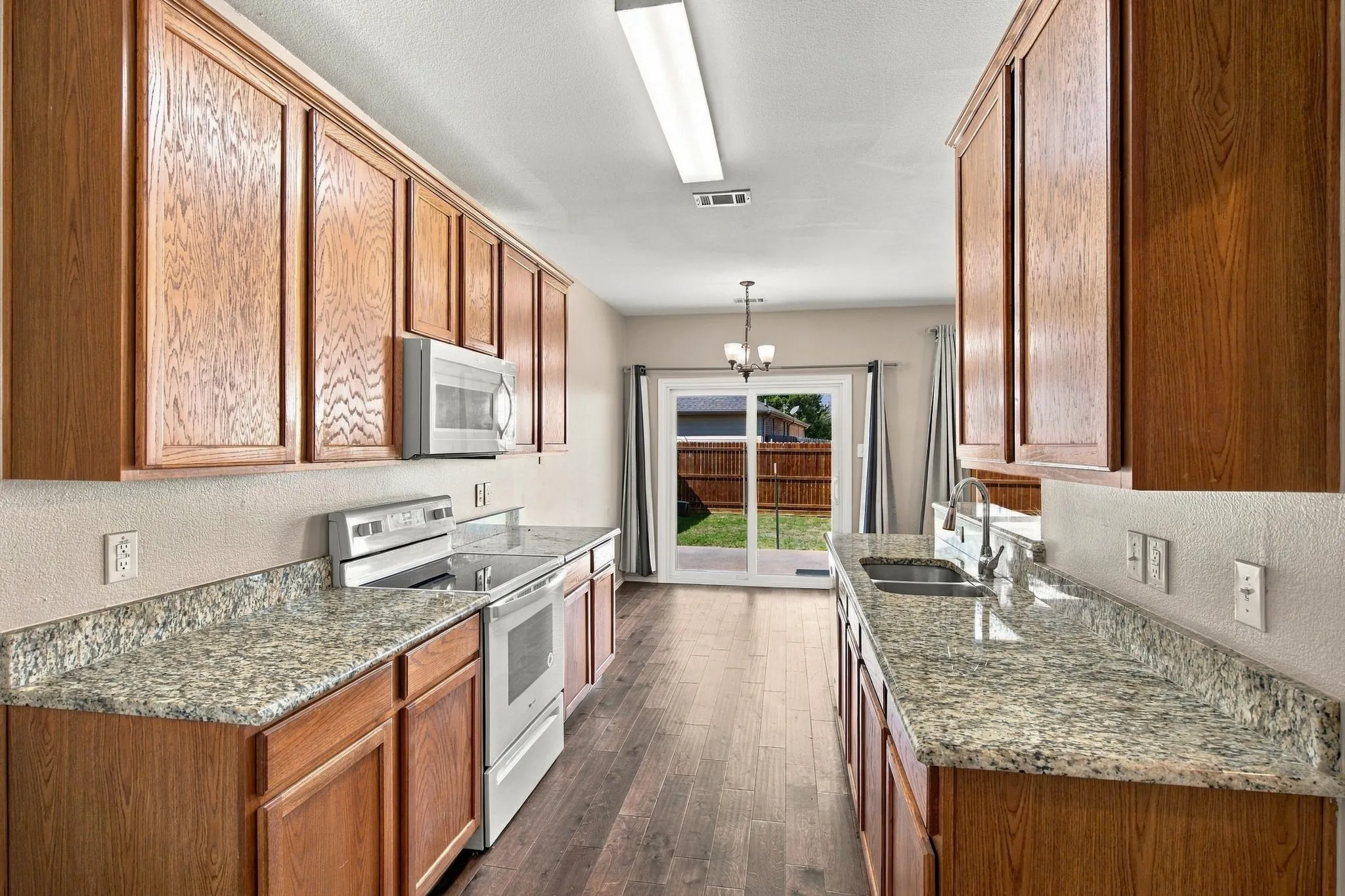 Kitchen featuring wood cabinetry, stone-finish countertops, stainless steel appliances, wood-finish flooring, and sliding glass doors