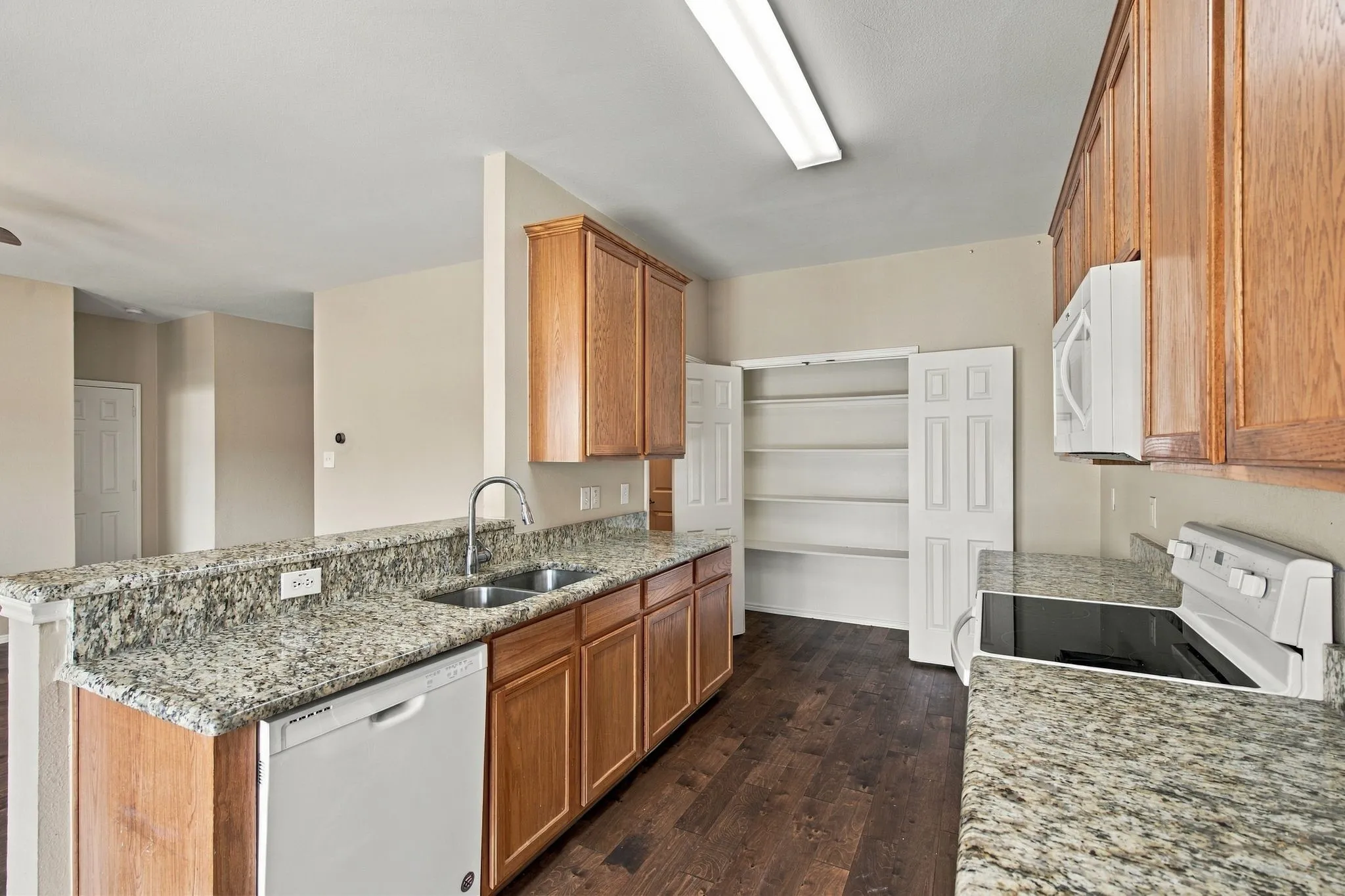 Kitchen featuring wood cabinetry, stone-surface countertops, wood-finish flooring, a double-basin stainless steel sink, and a walk-in pantry with bi-fold doors