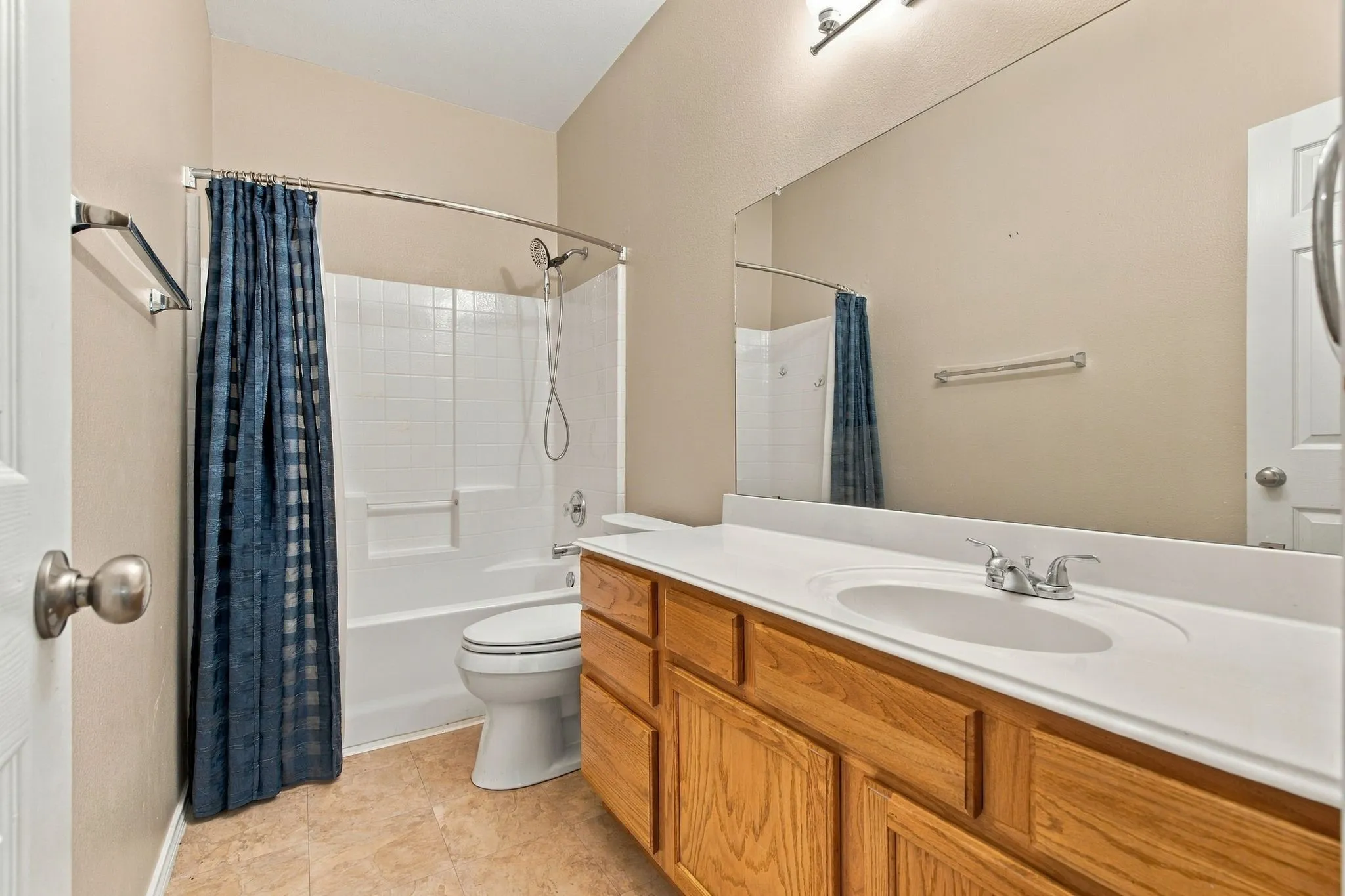 Bathroom featuring a wood-finish vanity with a white countertop and oval undermount sink, large wall-mounted mirror, and a tub-shower combination with tile surround