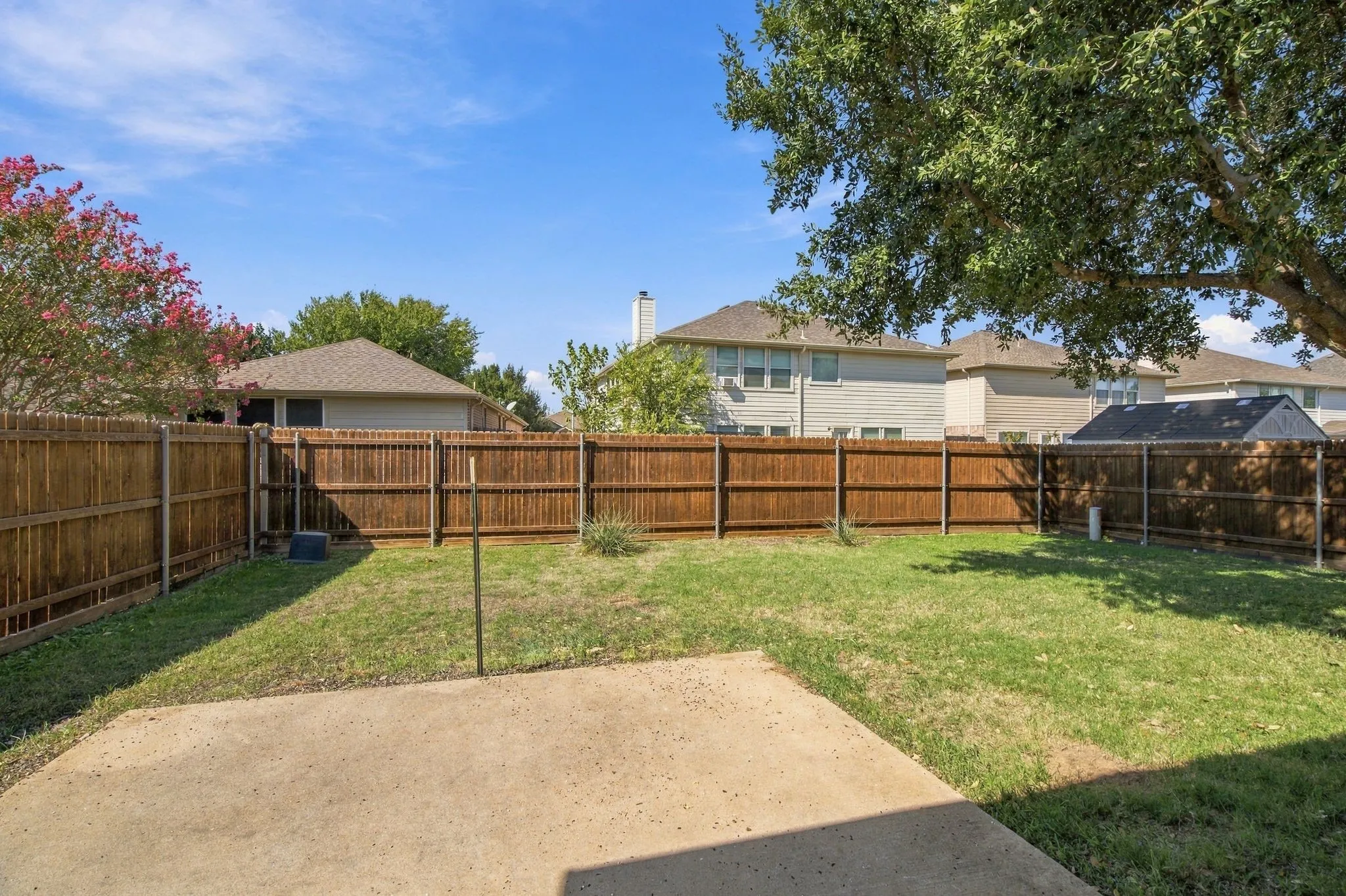 Fenced backyard featuring a concrete patio, grass lawn, and mature trees