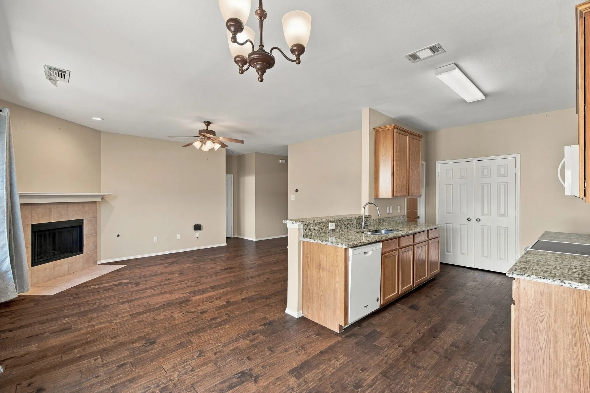 Wood-finish flooring, stone-surfaced peninsula with integrated cabinetry, built-in fireplace with tile surround, ceiling fan, and multi-arm chandelier