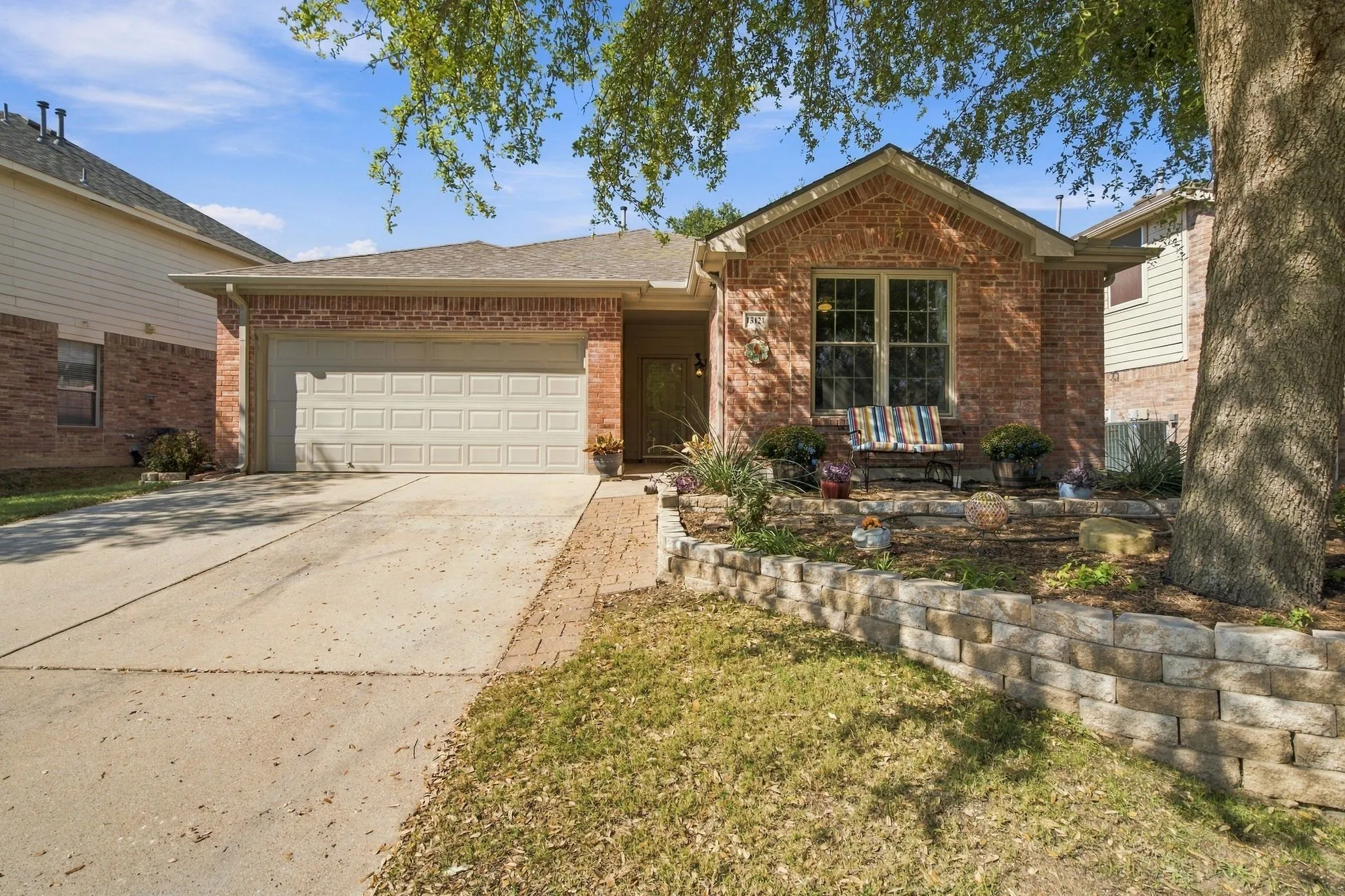 Single-story brick exterior featuring a multi-gable roofline, two-car garage, and tiered stone retaining wall