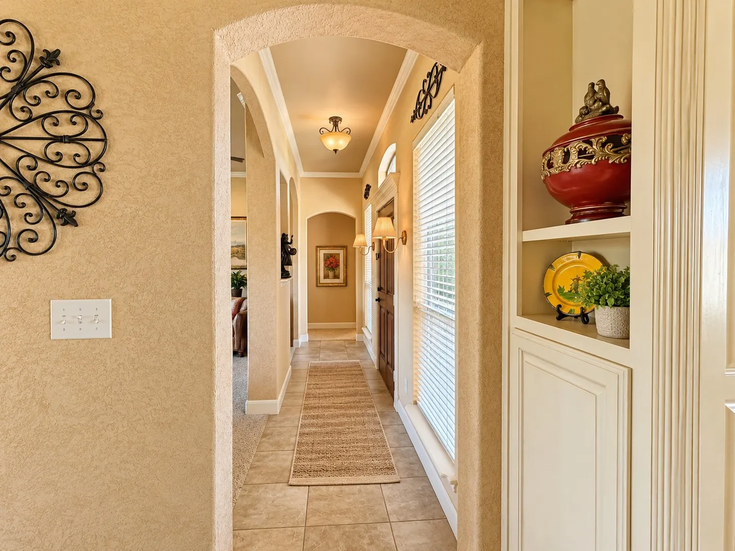Architectural archways, tile flooring, built-in recessed cabinetry, and traditional wall-mounted light fixtures
