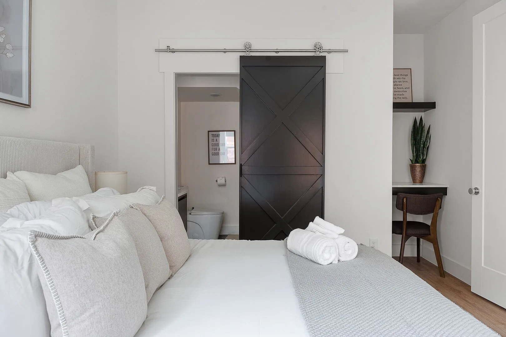 Dark-finished X-pattern sliding barn door with brushed metal hardware, built-in floating desk with stone surface, and wood-finish flooring