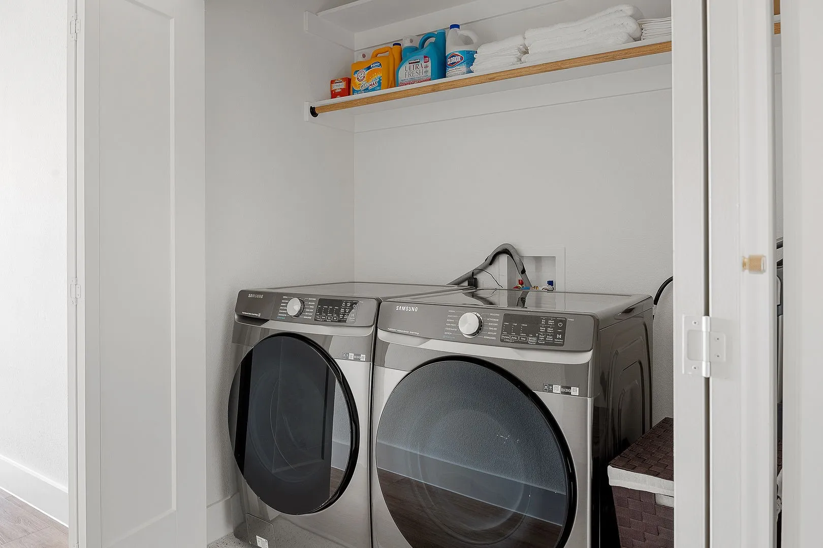 Laundry alcove featuring stainless steel front-load appliances and overhead built-in shelving