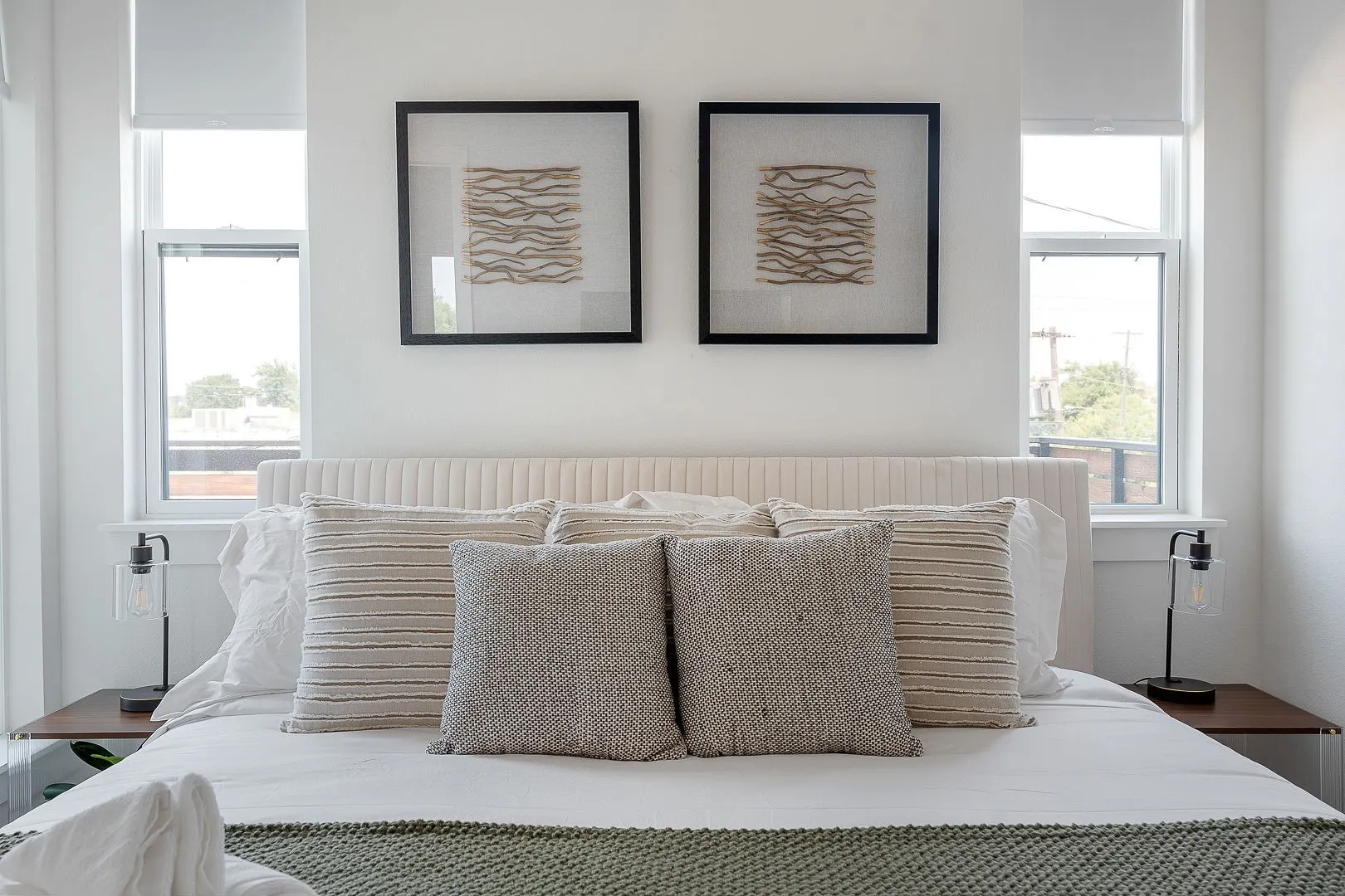 Dual vertical windows with roller shades, complemented by wall-mounted lighting fixtures on fixed wooden bedside platforms