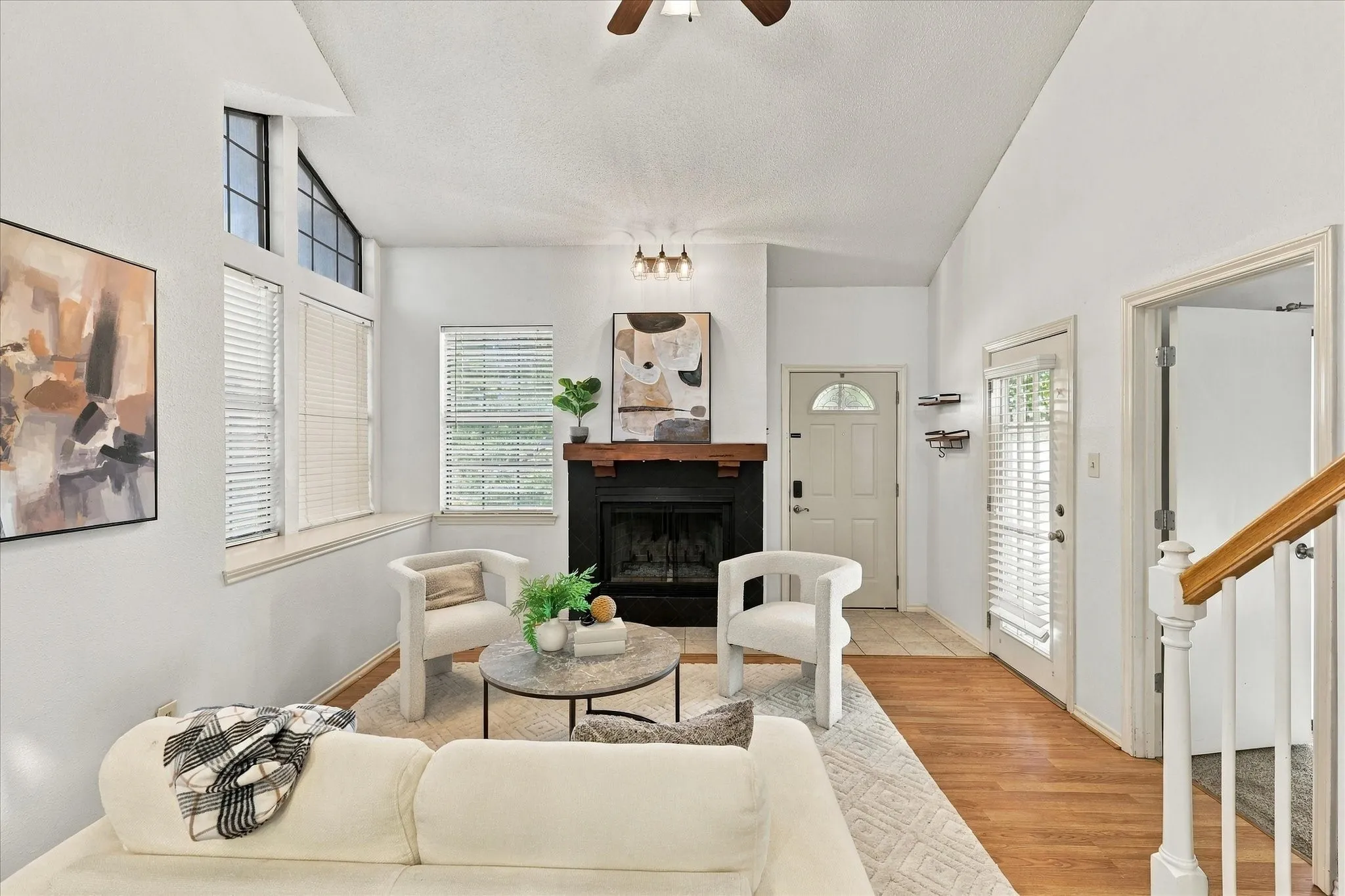 Vaulted ceilings with architectural windows, wood-finish flooring, and a fireplace featuring a substantial wooden mantel