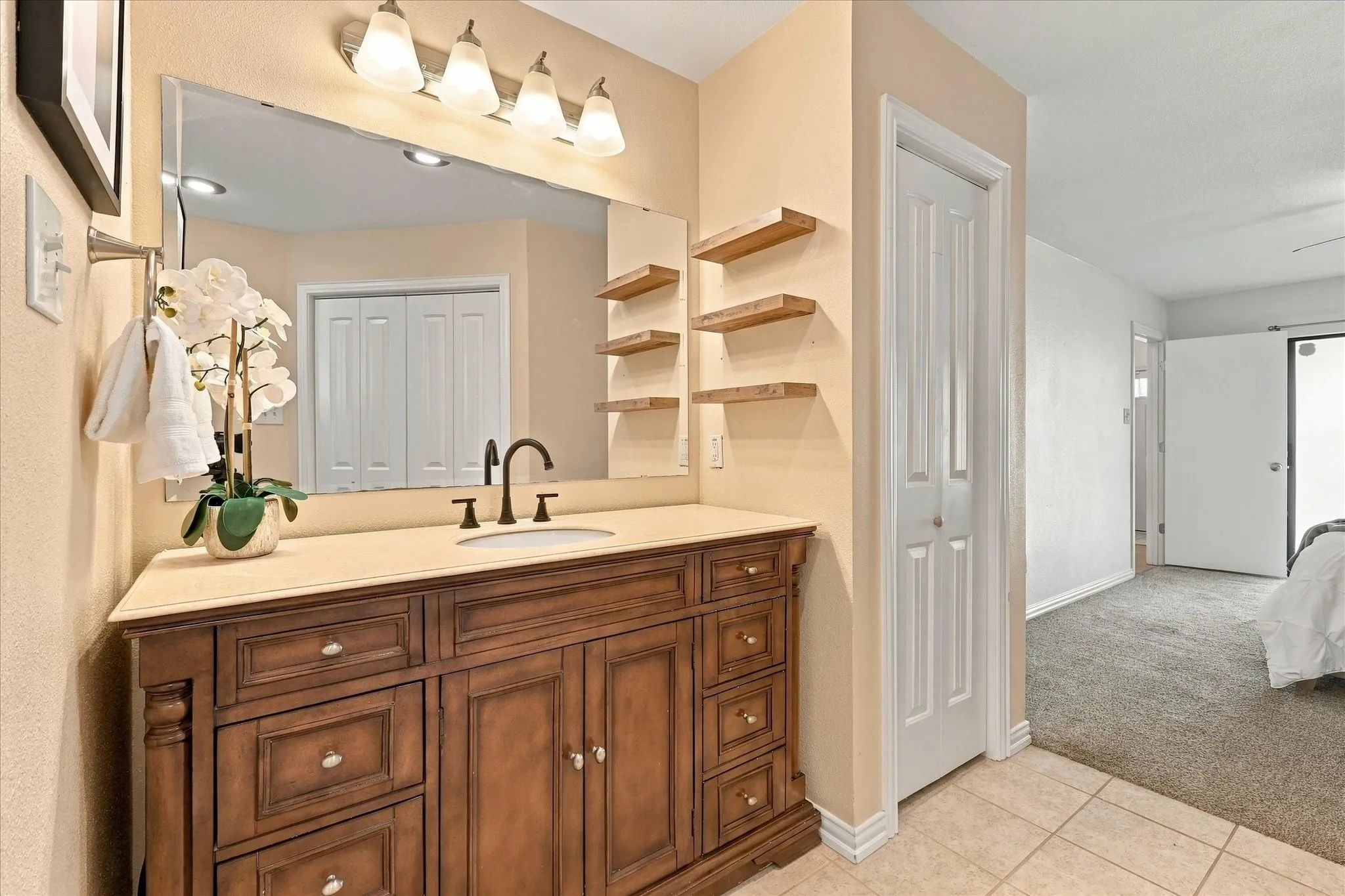 Bathroom vanity featuring dark-stained wood cabinetry, solid-surface countertop, undermount sink with dual-handle faucet, large wall-mounted mirror, and tiered wood floating shelves