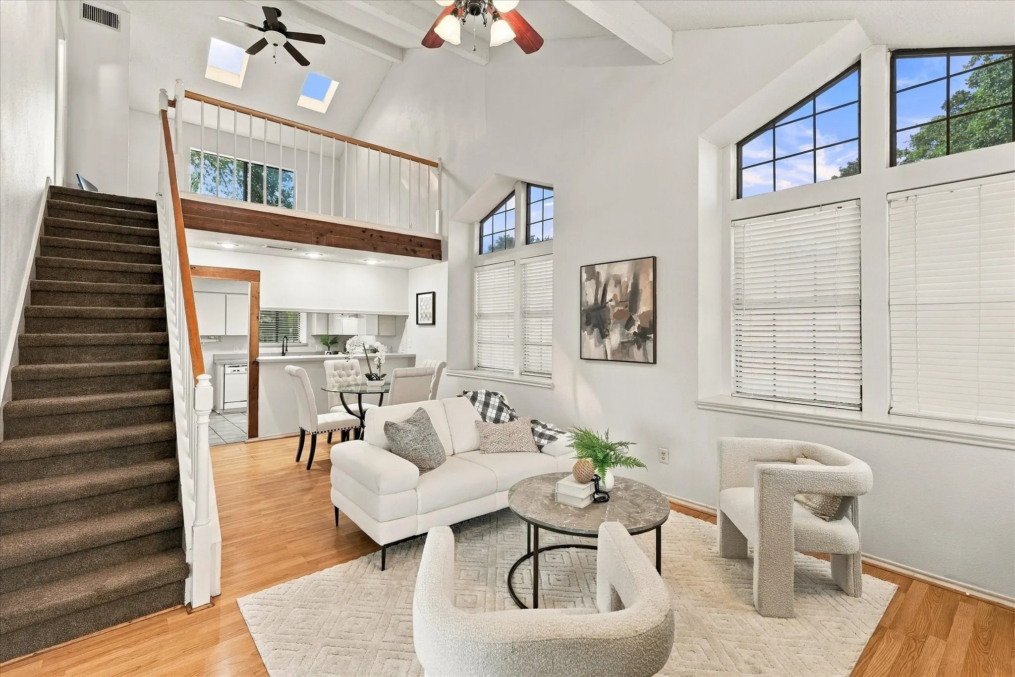Vaulted ceilings featuring exposed beams, floor-to-ceiling windows, skylights, and a wood-finish staircase with a white railing