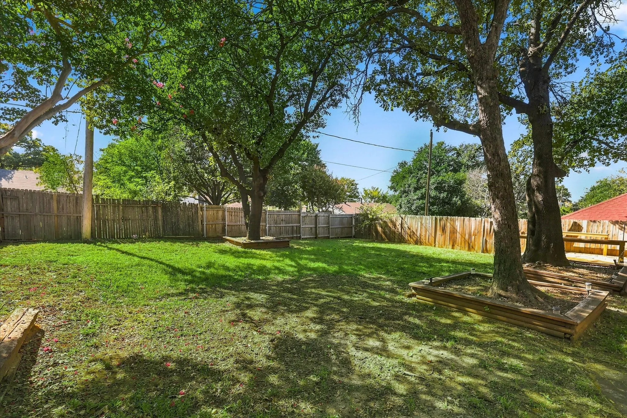 Backyard featuring a grass lawn, mature trees, wood privacy fencing, and raised timber tree beds