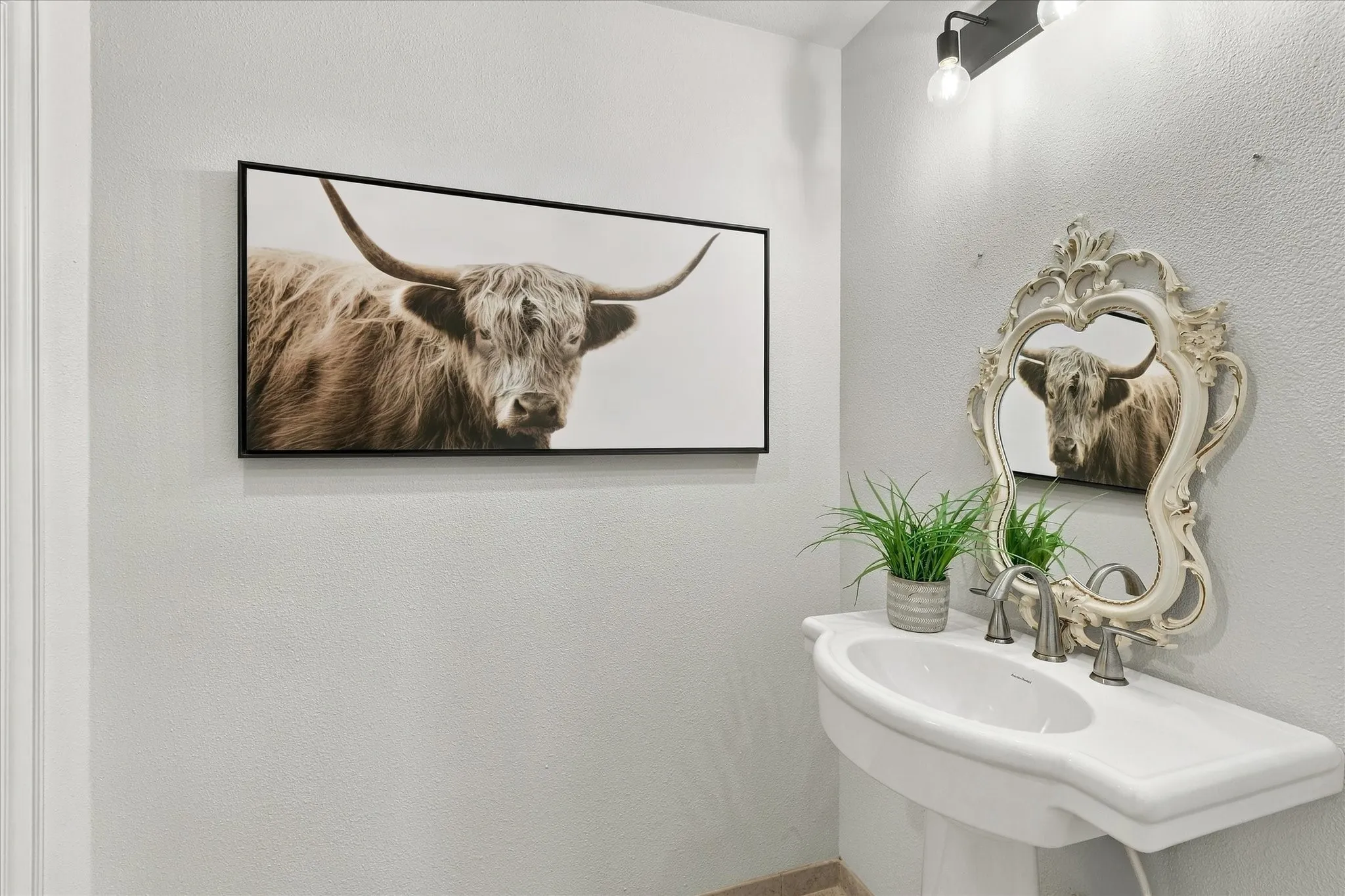 White porcelain pedestal sink with a metallic widespread faucet and a wall-mounted two-light fixture