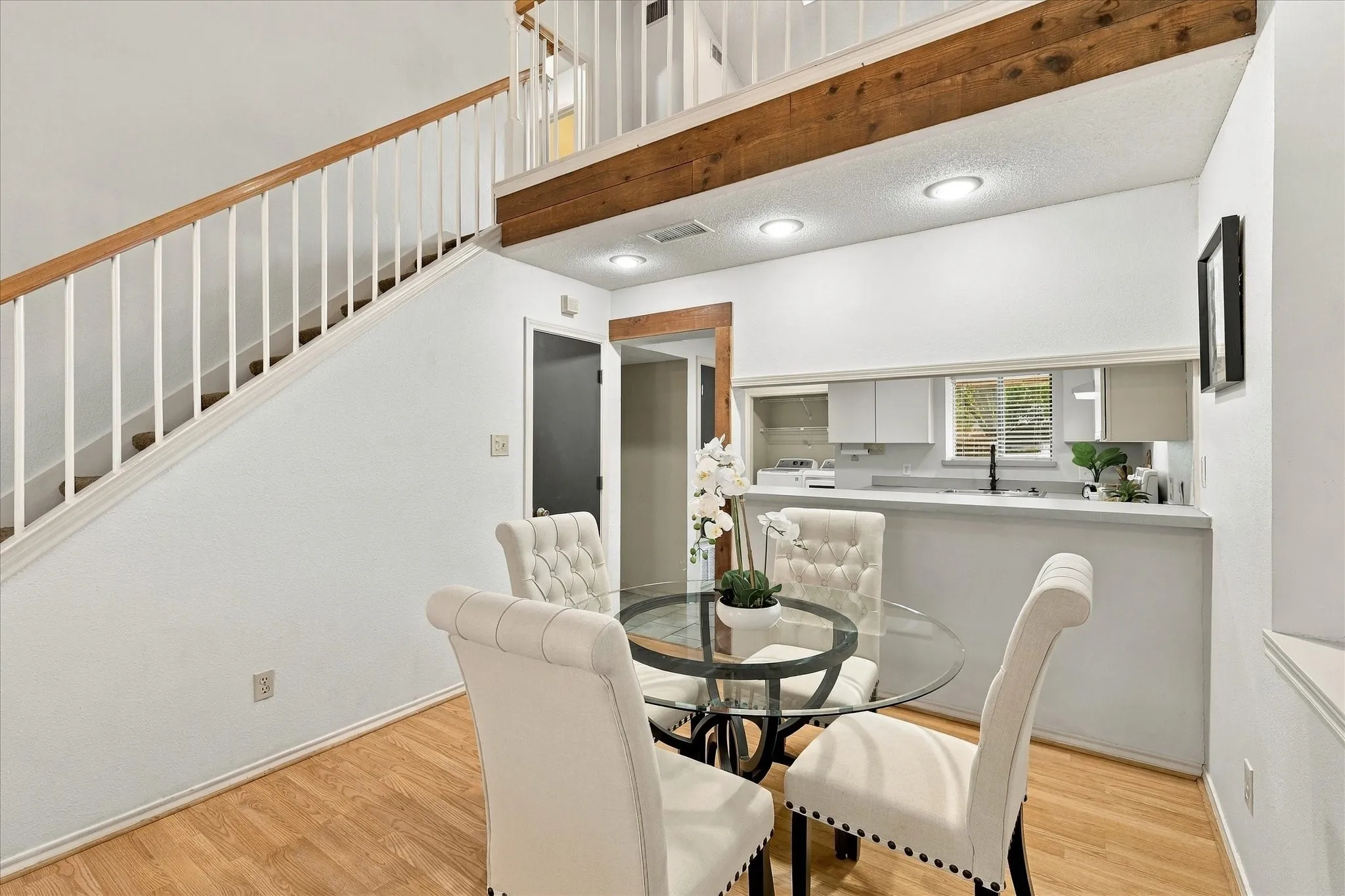 High ceilings with exposed wood beams, staircase featuring white metal balusters and wood handrail, recessed lighting, and kitchen pass-through with wood-finish flooring