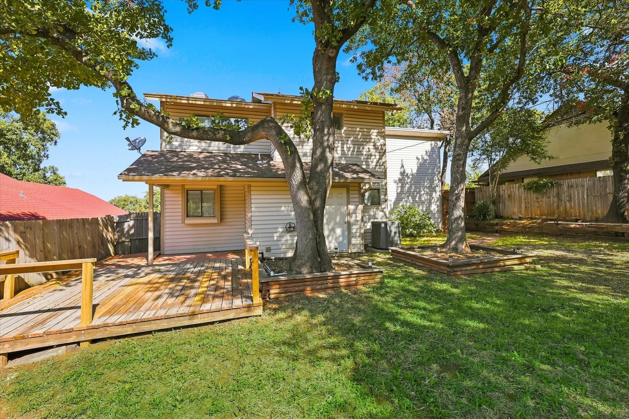 Backyard featuring a wood-plank deck, mature trees, raised garden beds, and wood privacy fencing