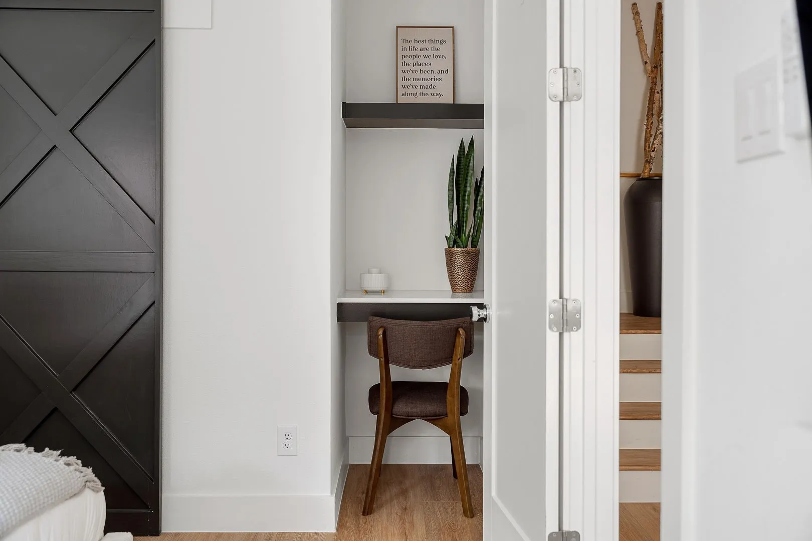 Built-in alcove featuring a floating desk, overhead shelving, wood-finish flooring, and a sliding barn-style door with a cross-brace design