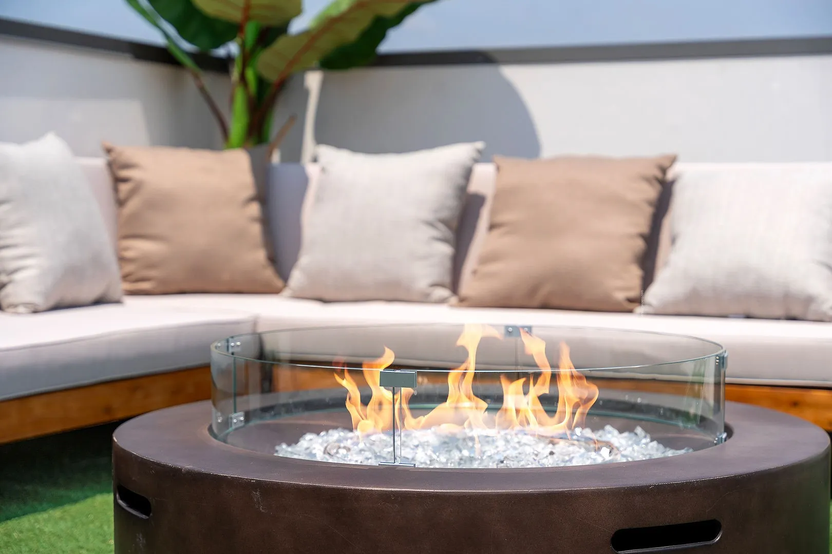 Circular fire pit featuring a smooth dark-toned base, integrated glass wind guard, and decorative stone filler