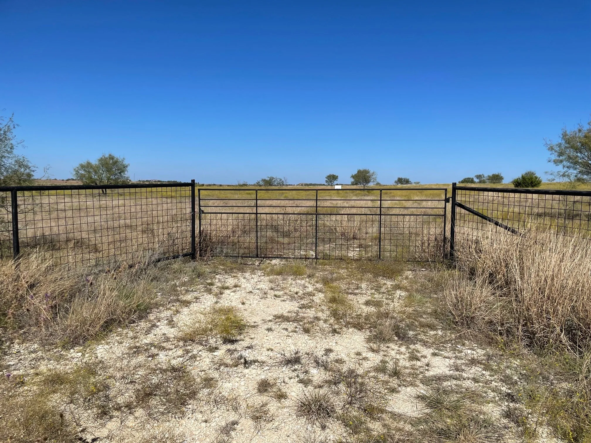Expansive acreage enclosed by metal wire perimeter fencing and a central metal gate