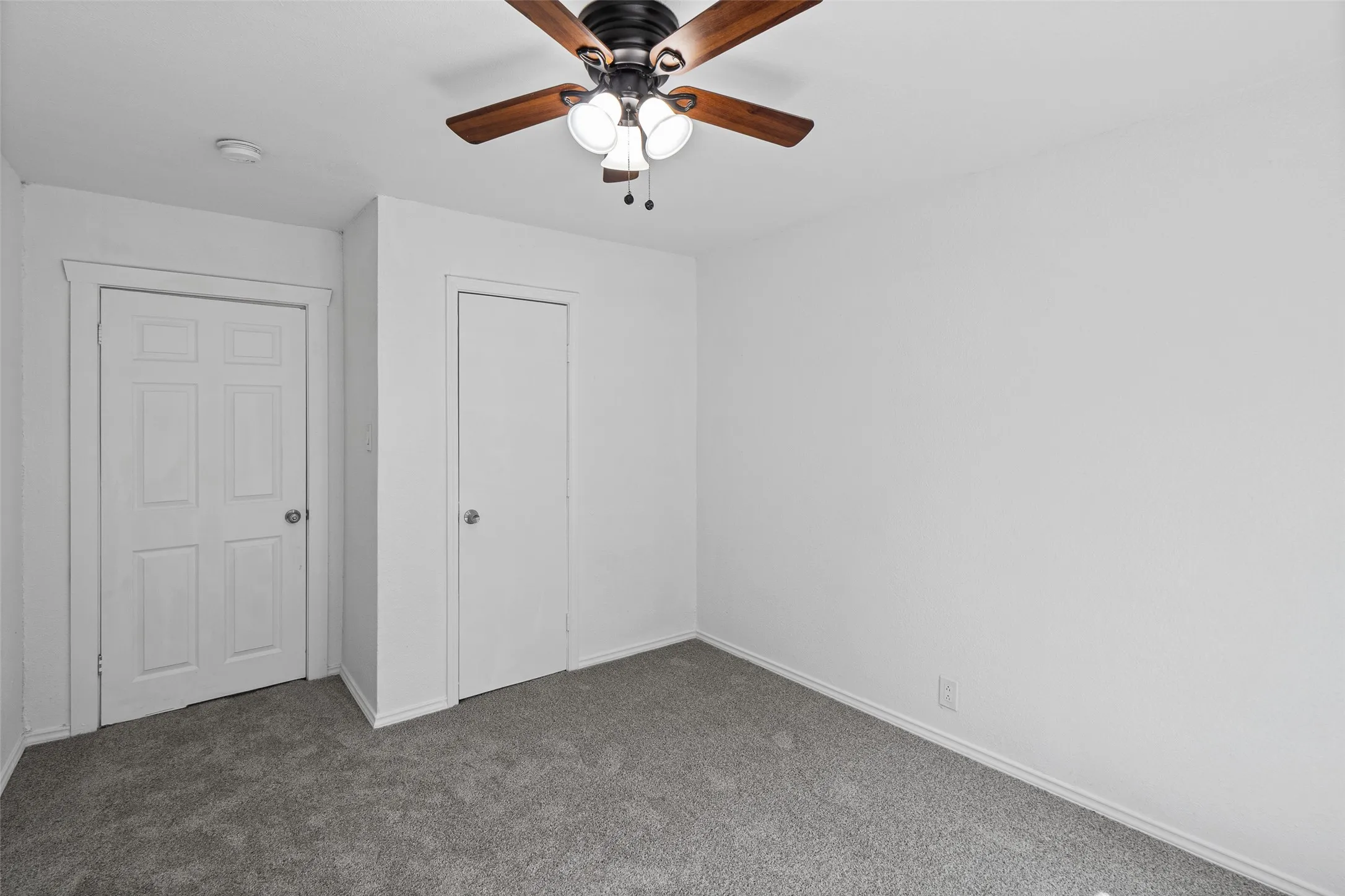 Interior space featuring neutral wall tones, gray carpeting, a multi-panel door, a closet with a single-panel door, and a ceiling fan with integrated lighting