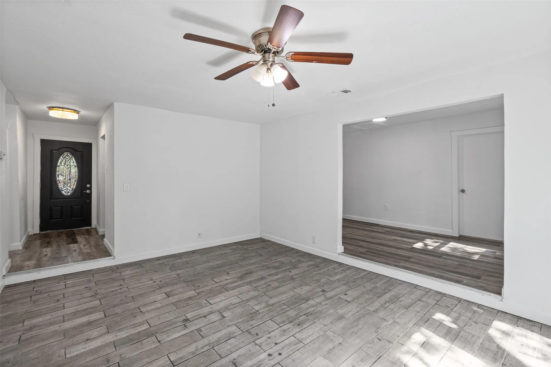 Interior featuring wood-finish tile flooring, a multi-blade ceiling fan with integrated lighting, and a black exterior door with decorative oval glass insert