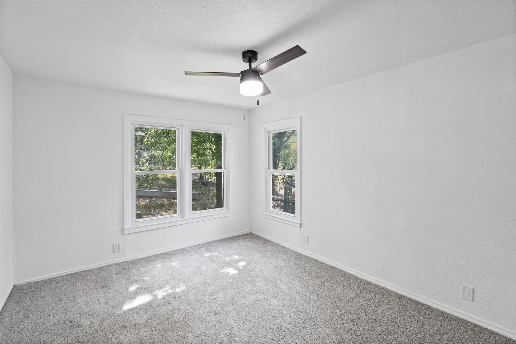 Interior space featuring neutral wall tones, wall-to-wall carpeting, a multi-pane window configuration, and a central ceiling fan with integrated lighting