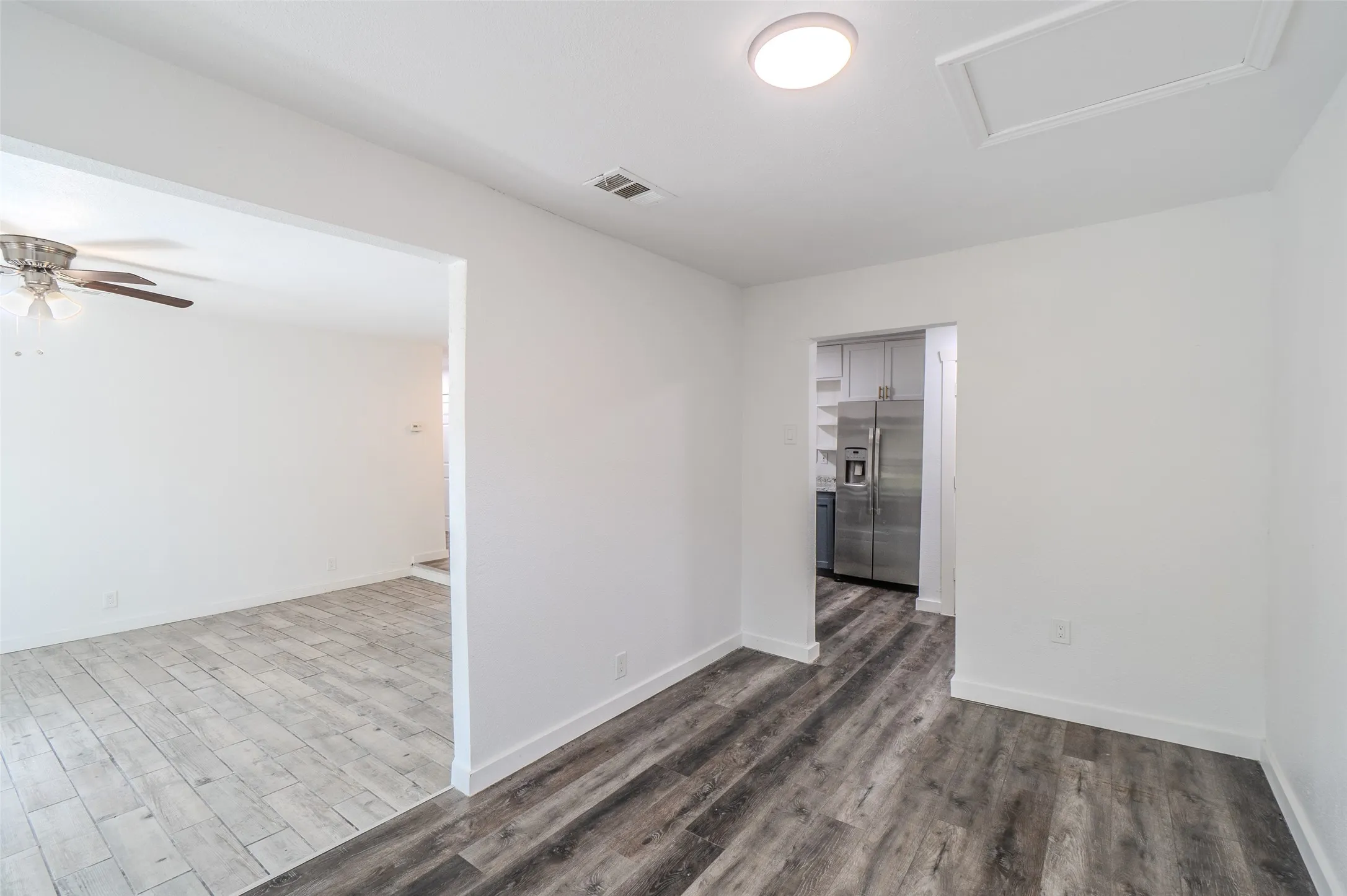 Open-concept interior featuring wood-finish flooring, recessed ceiling lighting, and a stainless steel refrigerator