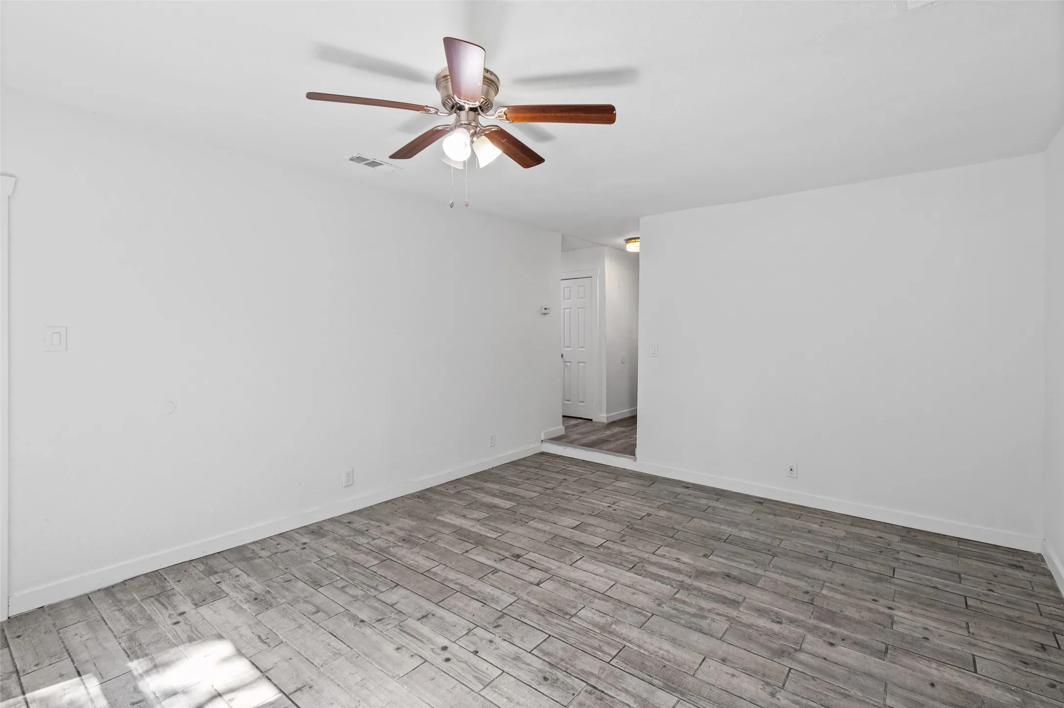 Interior space featuring wood-finish tile flooring, white walls, and a ceiling-mounted fan with integrated light fixture
