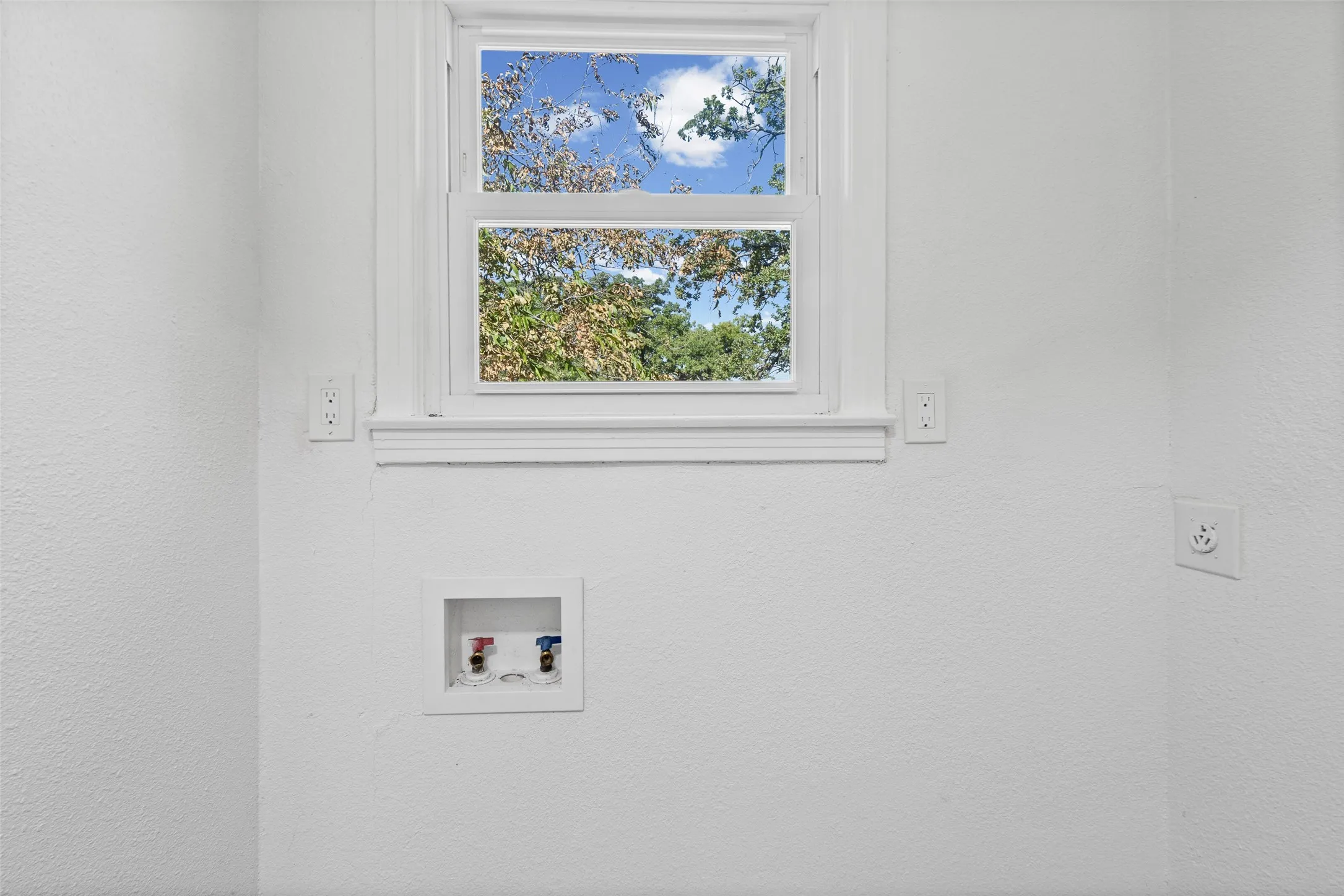 Single-hung window with white casing, recessed water supply box, and dedicated electrical outlets for washer and dryer equipment