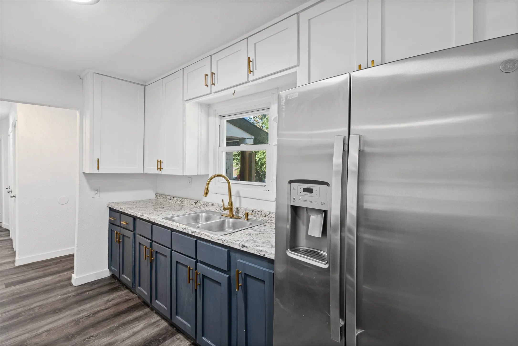 Kitchen featuring two-tone shaker cabinetry, stone-finish countertops, stainless steel side-by-side refrigerator, gold-tone hardware, and dual-basin sink with a matching gooseneck faucet