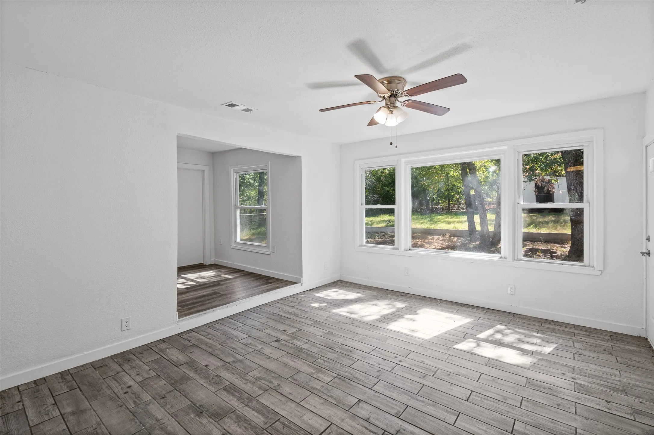 Neutral interior featuring wood-finish flooring, a ceiling fan with integrated lighting, and expansive windows