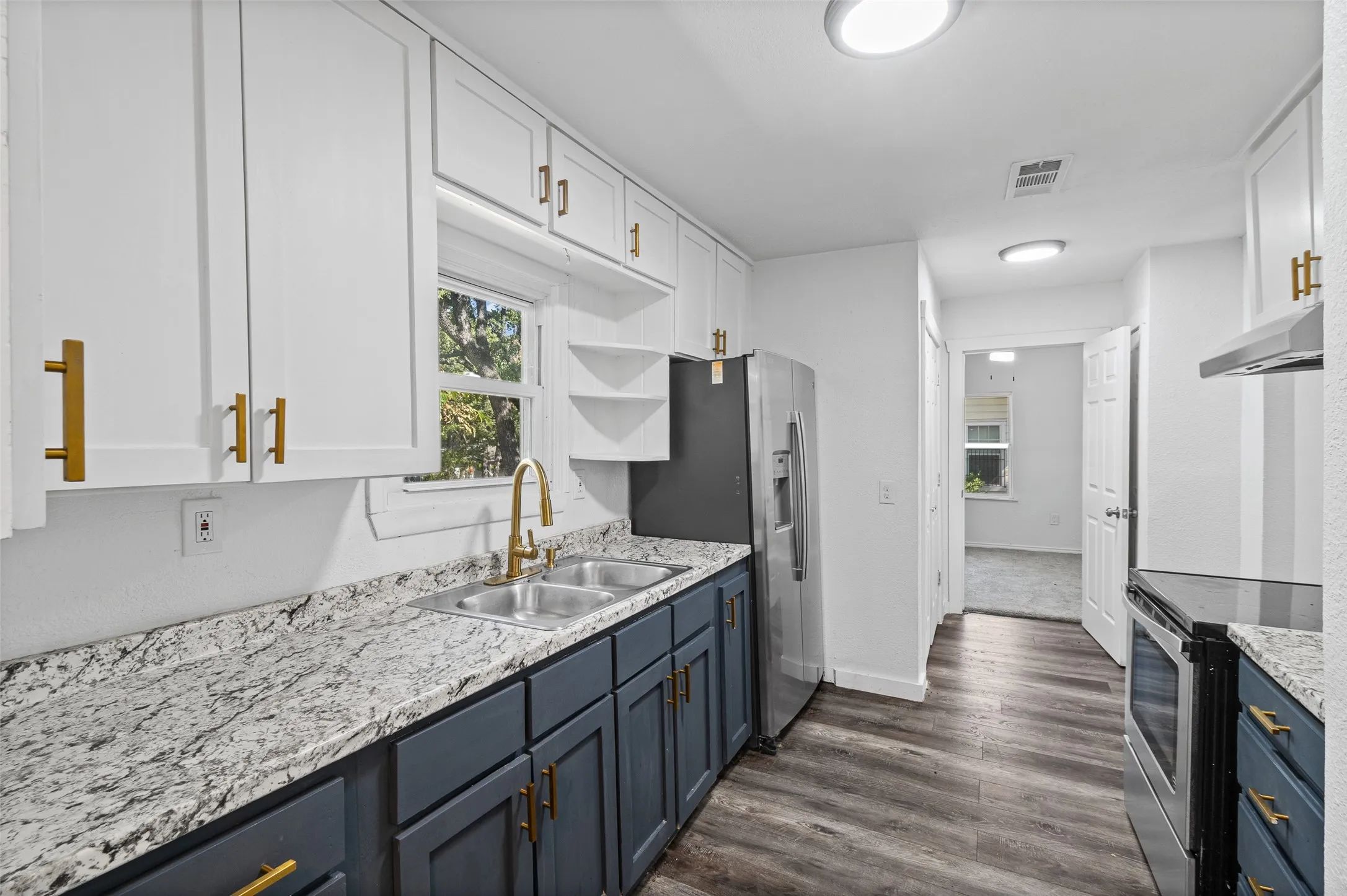 Kitchen featuring two-tone cabinetry with gold-toned hardware, stone-patterned countertops, dual-basin stainless steel sink with a high-arch faucet, and wood-finish flooring