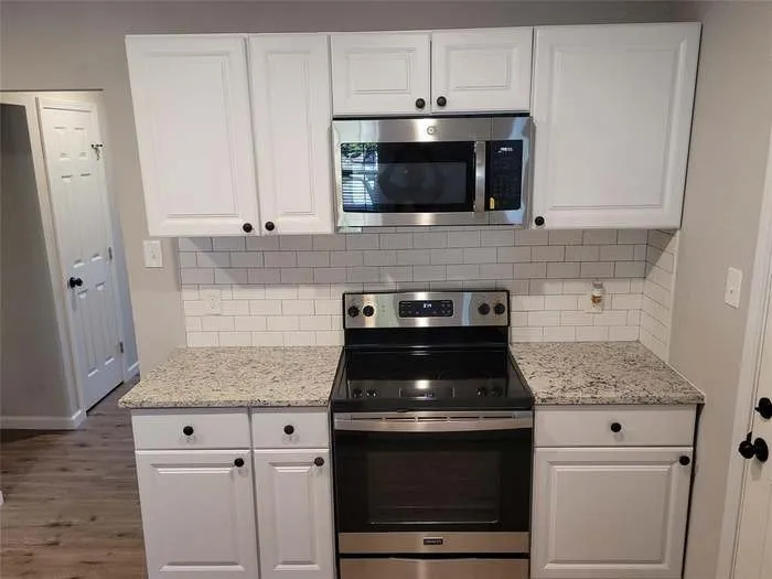 Kitchen featuring white shaker-style cabinetry, speckled stone-finish countertops, stainless steel microwave, stainless steel range, and subway tile backsplash