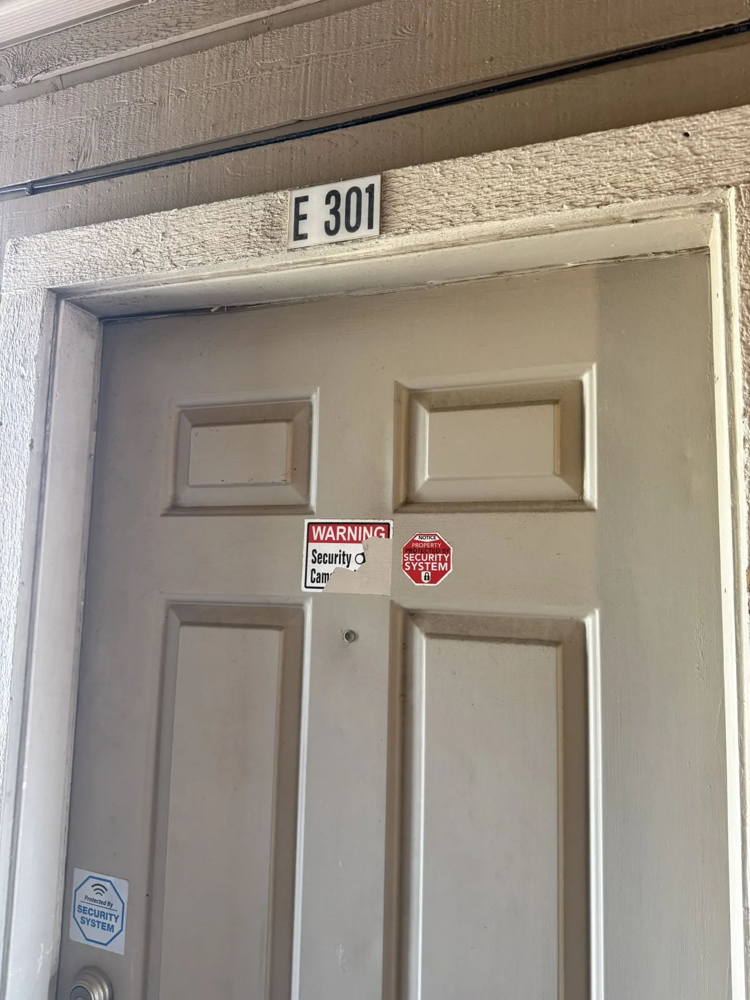 Entry door featuring a six-panel design and a door-mounted peephole, positioned beneath a unit number identification plaque