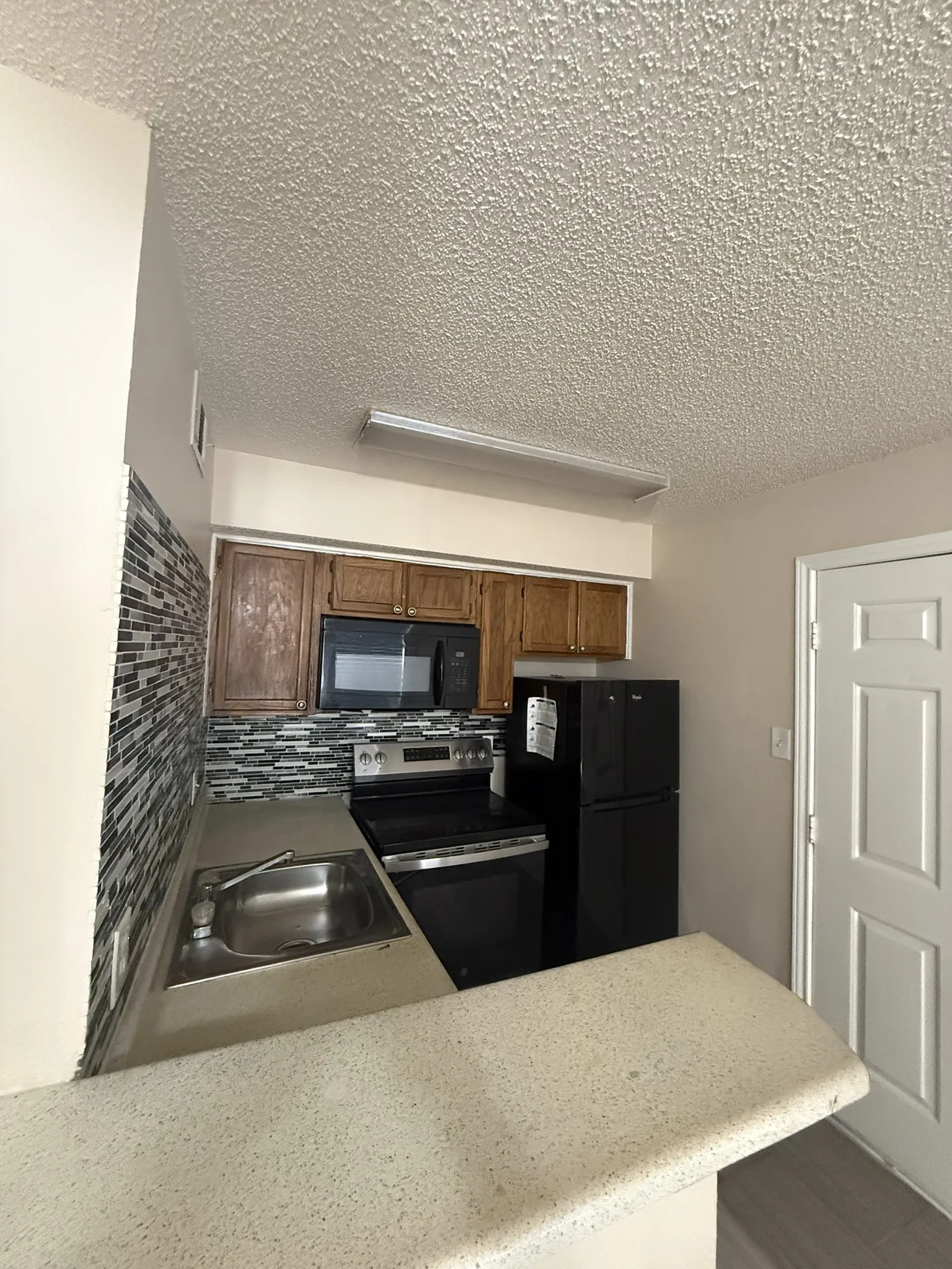 Kitchen featuring wood cabinetry, a decorative tile backsplash, stone-finish countertops, and black built-in appliances including a microwave, range, and refrigerator