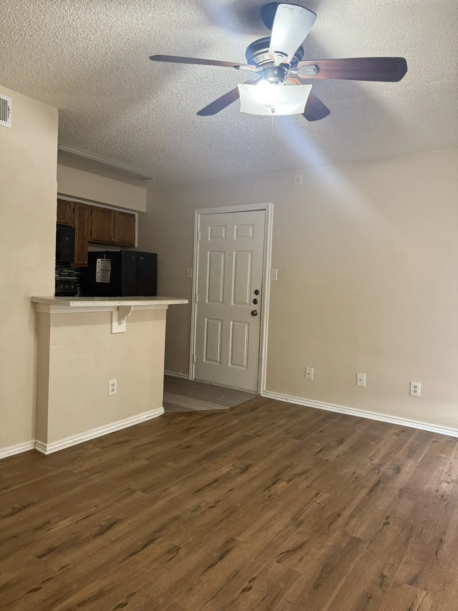 Wood-finish flooring, breakfast bar with a solid surface countertop, wooden cabinetry, and a ceiling fan with integrated lighting