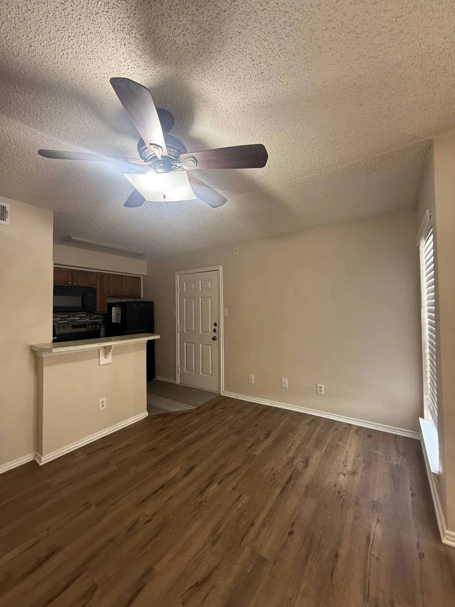 Wood-finish flooring, ceiling fan with integrated lighting, window with horizontal blinds, built-in breakfast bar, and panel-style entry door
