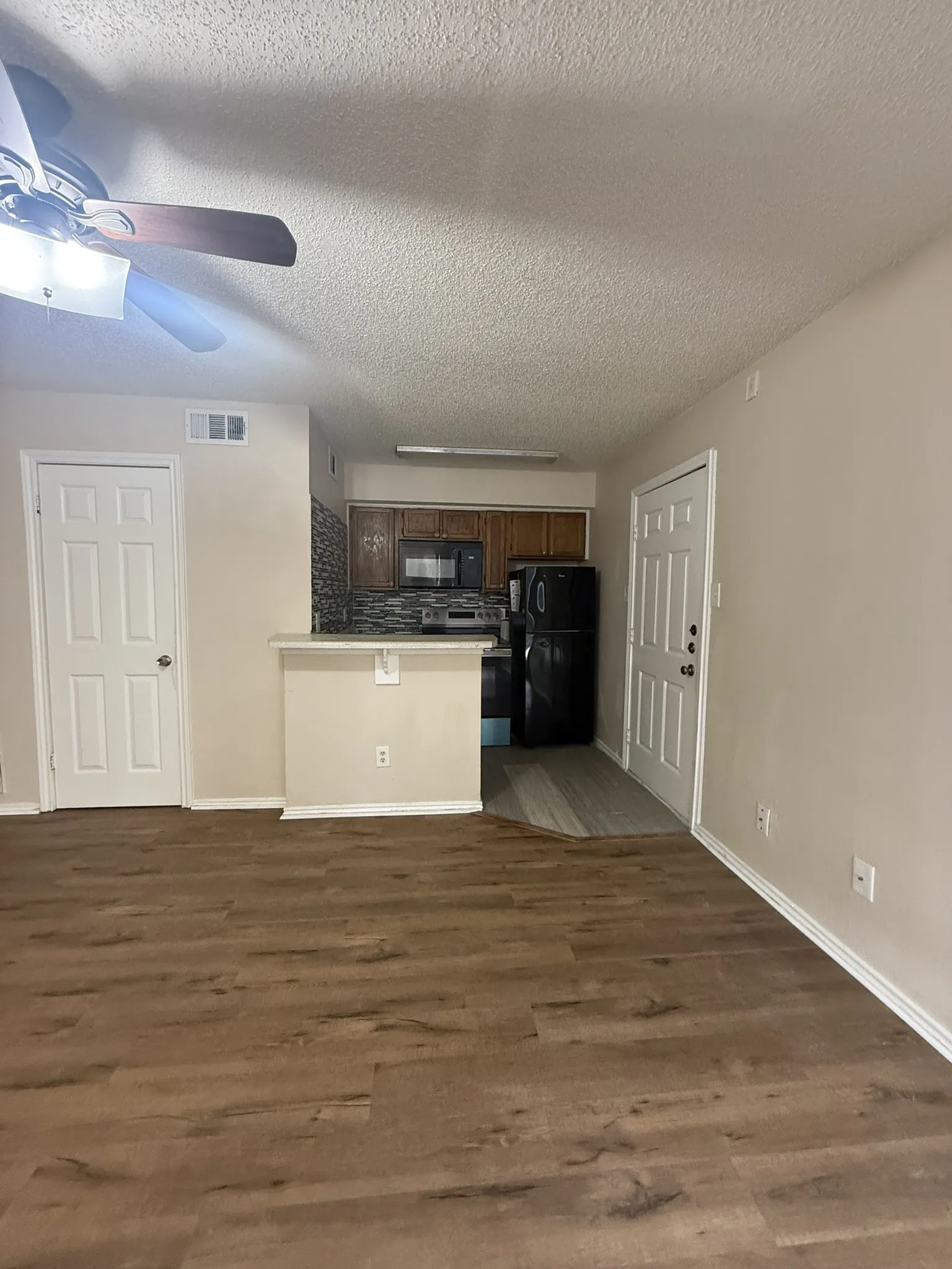 Kitchen featuring wood-finish cabinetry, black appliances, stone-patterned backsplash, and a breakfast bar, complemented by wood-finish flooring and a ceiling fan