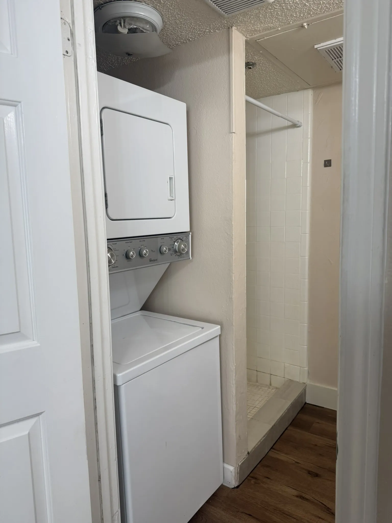 Stacked laundry center featuring a white washer and dryer, tile-surround shower, and wood-finish flooring