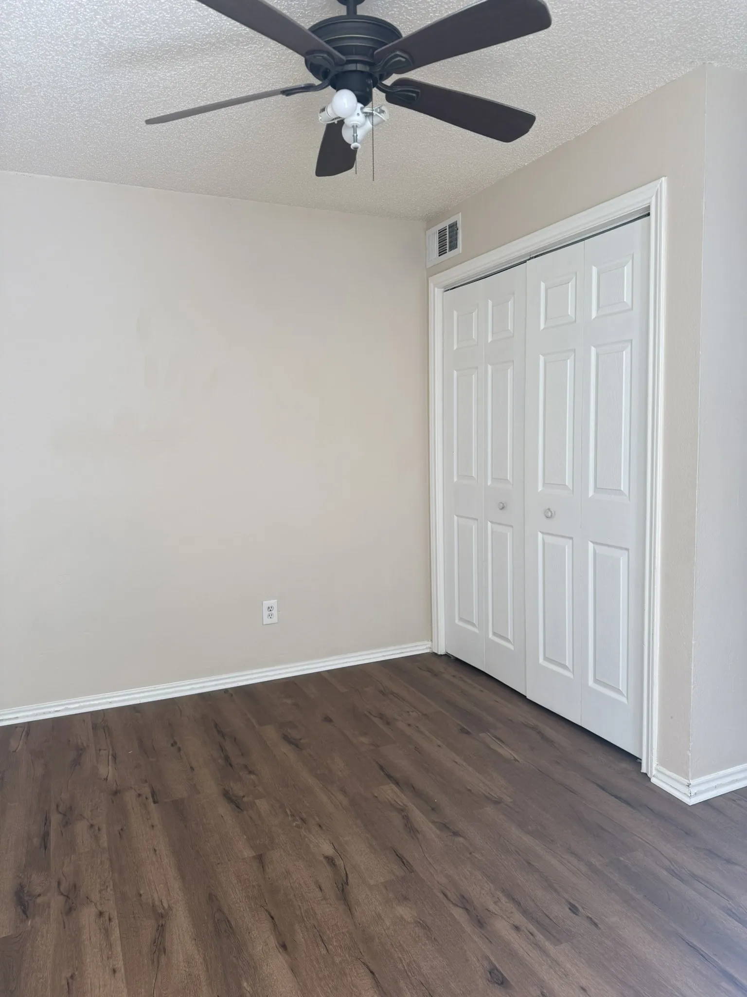 Room featuring wood-finish flooring, a ceiling fan with integrated lighting, and a dual-panel closet door